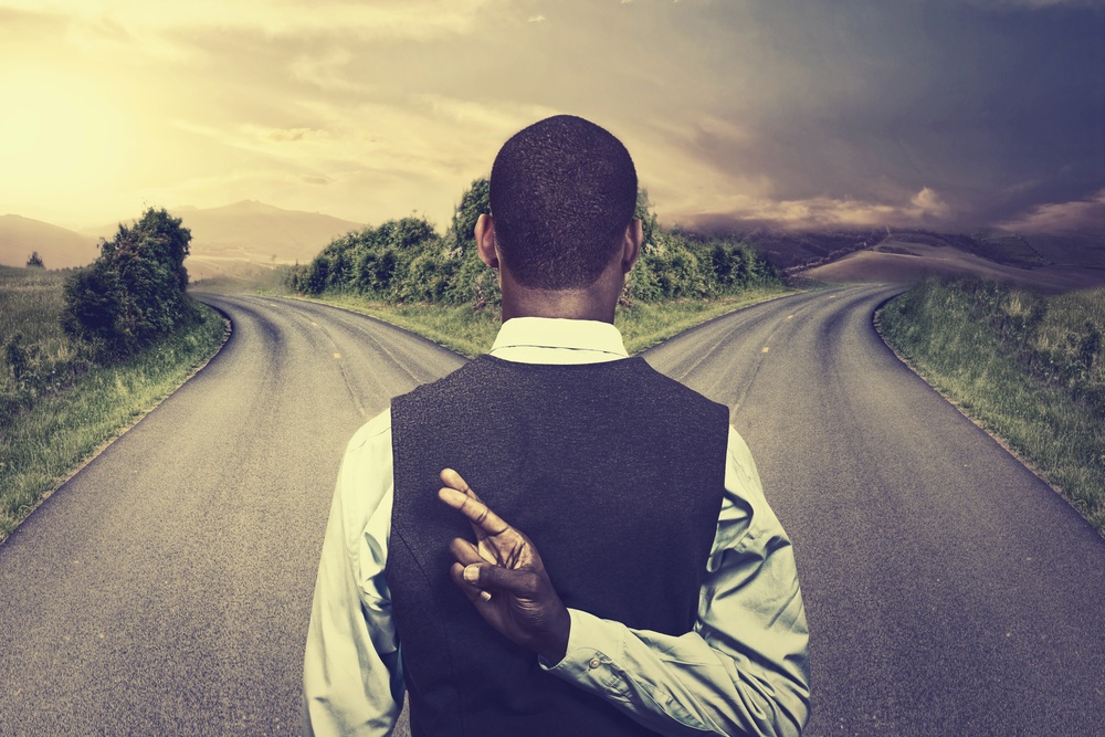businessman in front of two roads crossing fingers hoping for best taking chance .jpeg