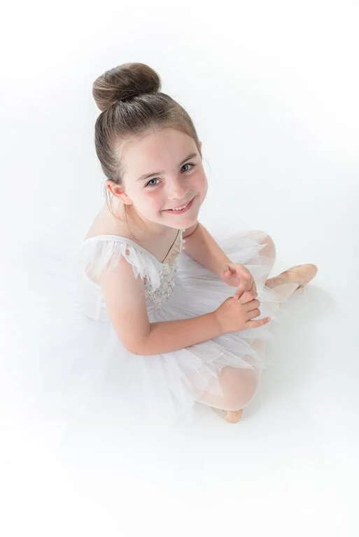 Smiling young girl in white ballet tutu looking up to camera