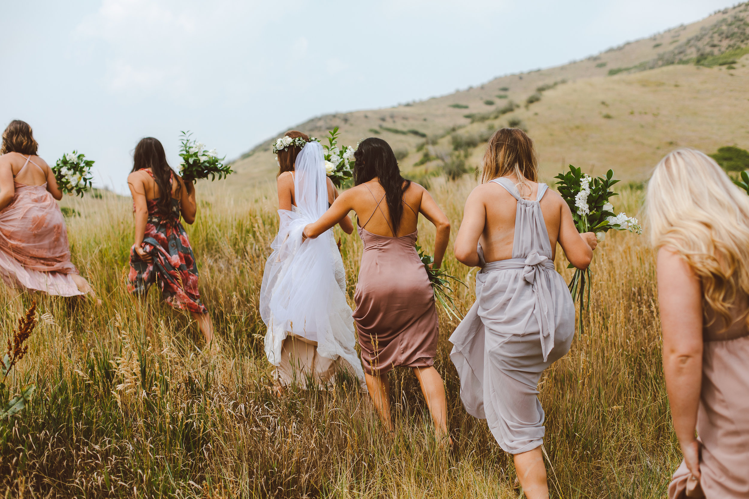 Bridesmaids helping bride through a field in Denver, Colorado