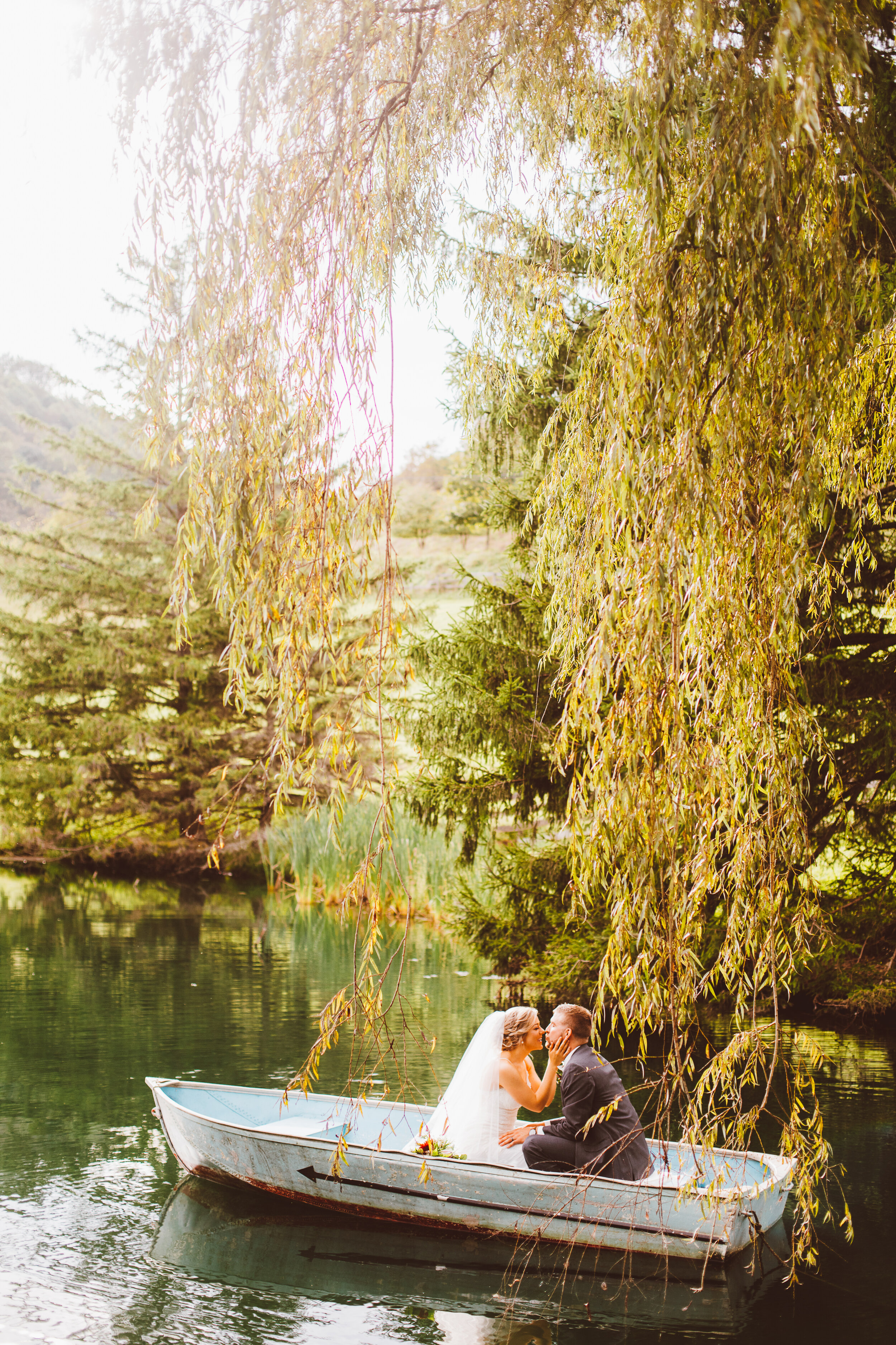 Bride and groom kissing in boat on lake with willow trees in Maryland