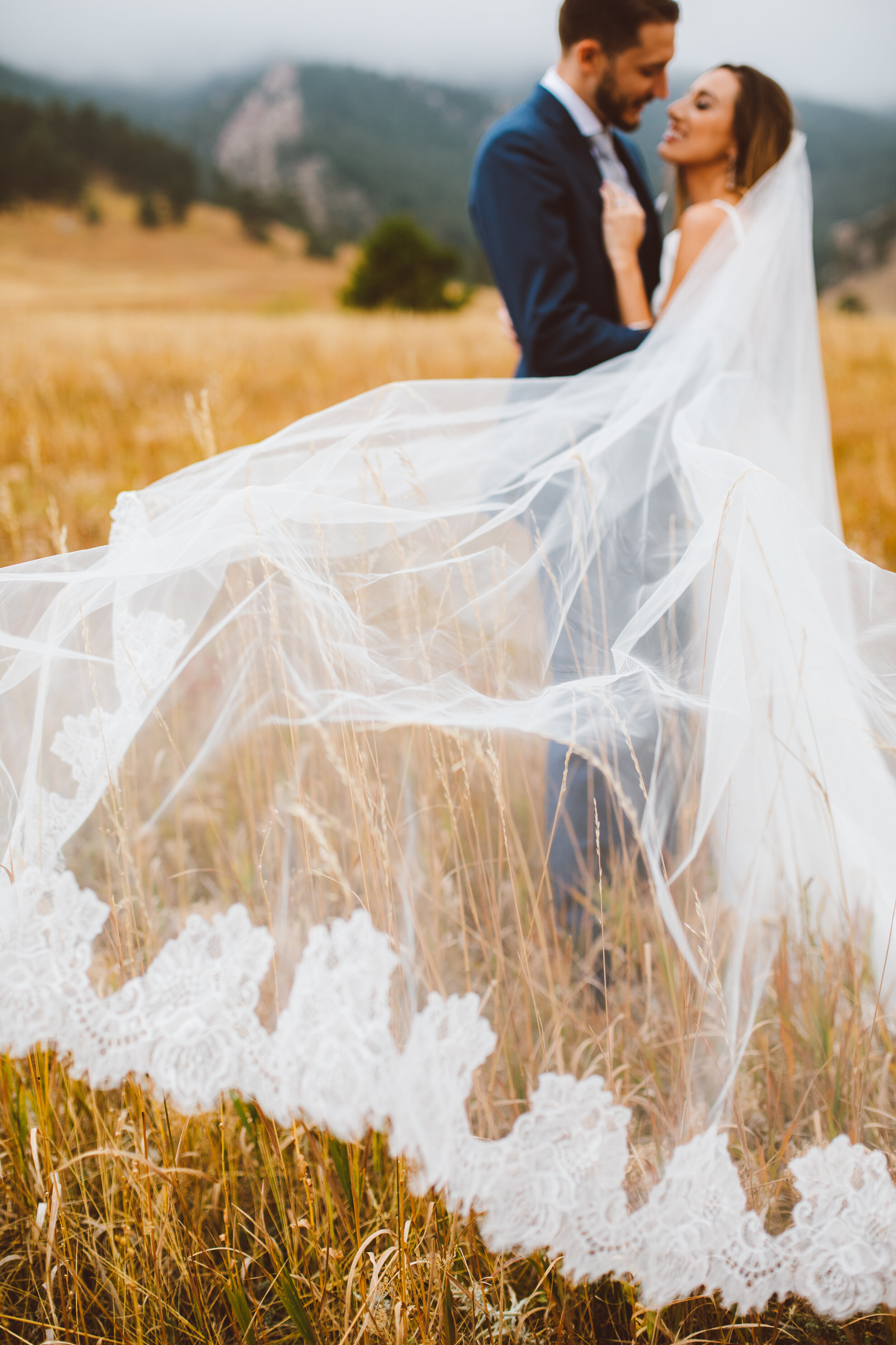 Long wedding veil in field with bride and groom