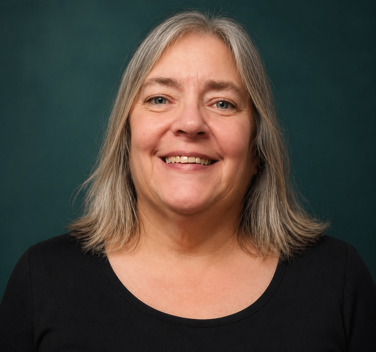 A middle-aged woman with shoulder-length gray hair smiling at the camera, wearing a black top, standing against a plain white background.