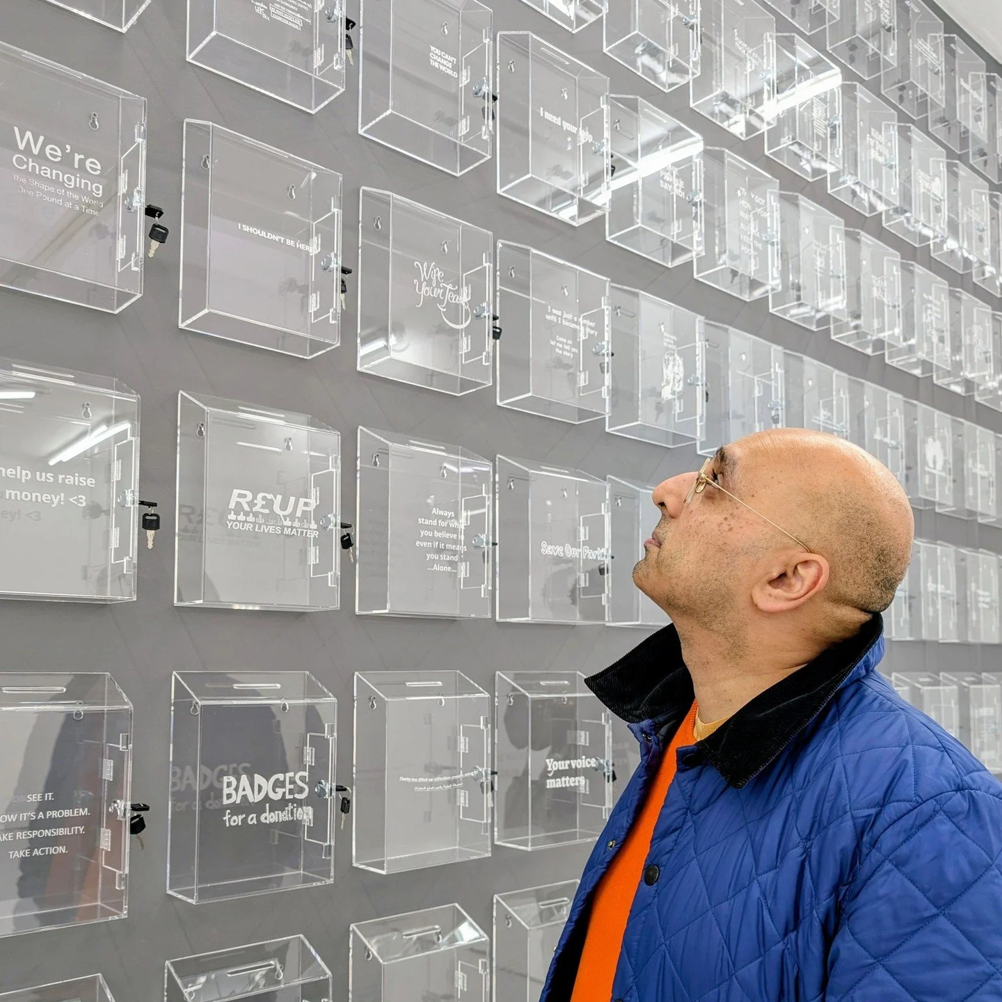 The wall is covered in transparent donation boxes. They are all based on leaflets the artist duo have received, ranging from serious topics such as freedom for Palestine and stopping knife crime to more personal requests and some that may be scams. I