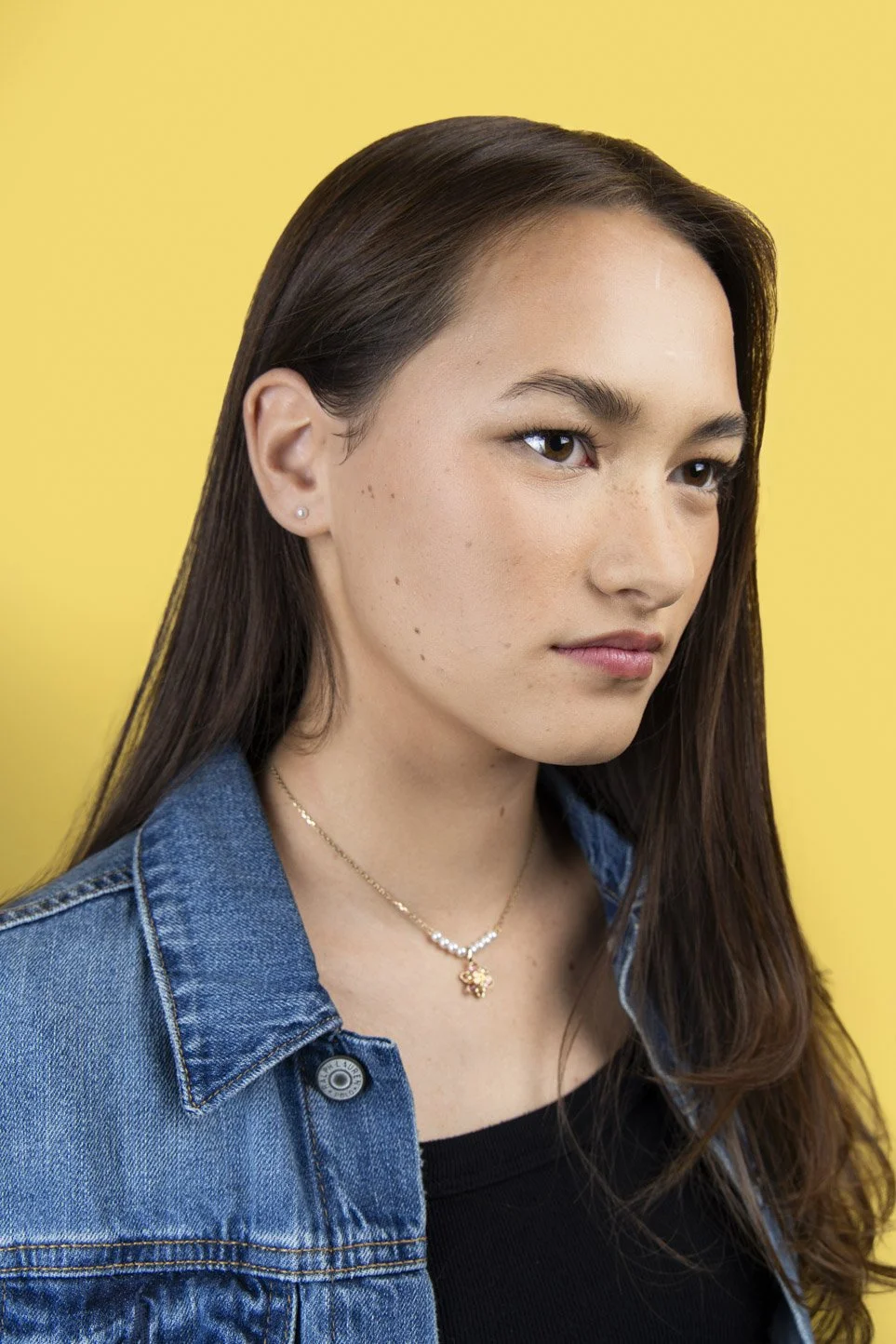 Mid-length modeling portfolio portrait of Gretchen in a jean jacket against a bright yellow backdrop