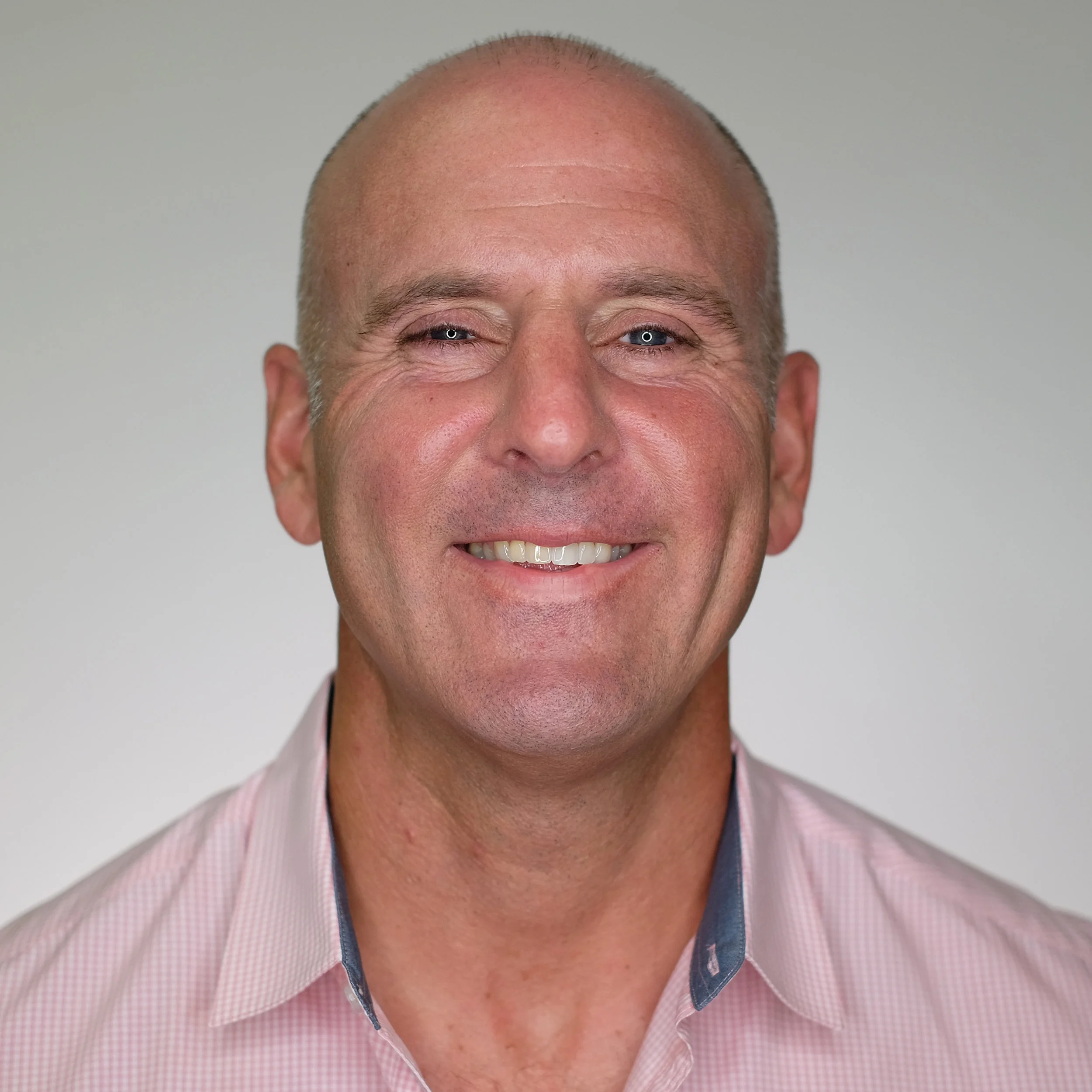 Close-up portrait of a smiling bald man wearing a pink collared shirt