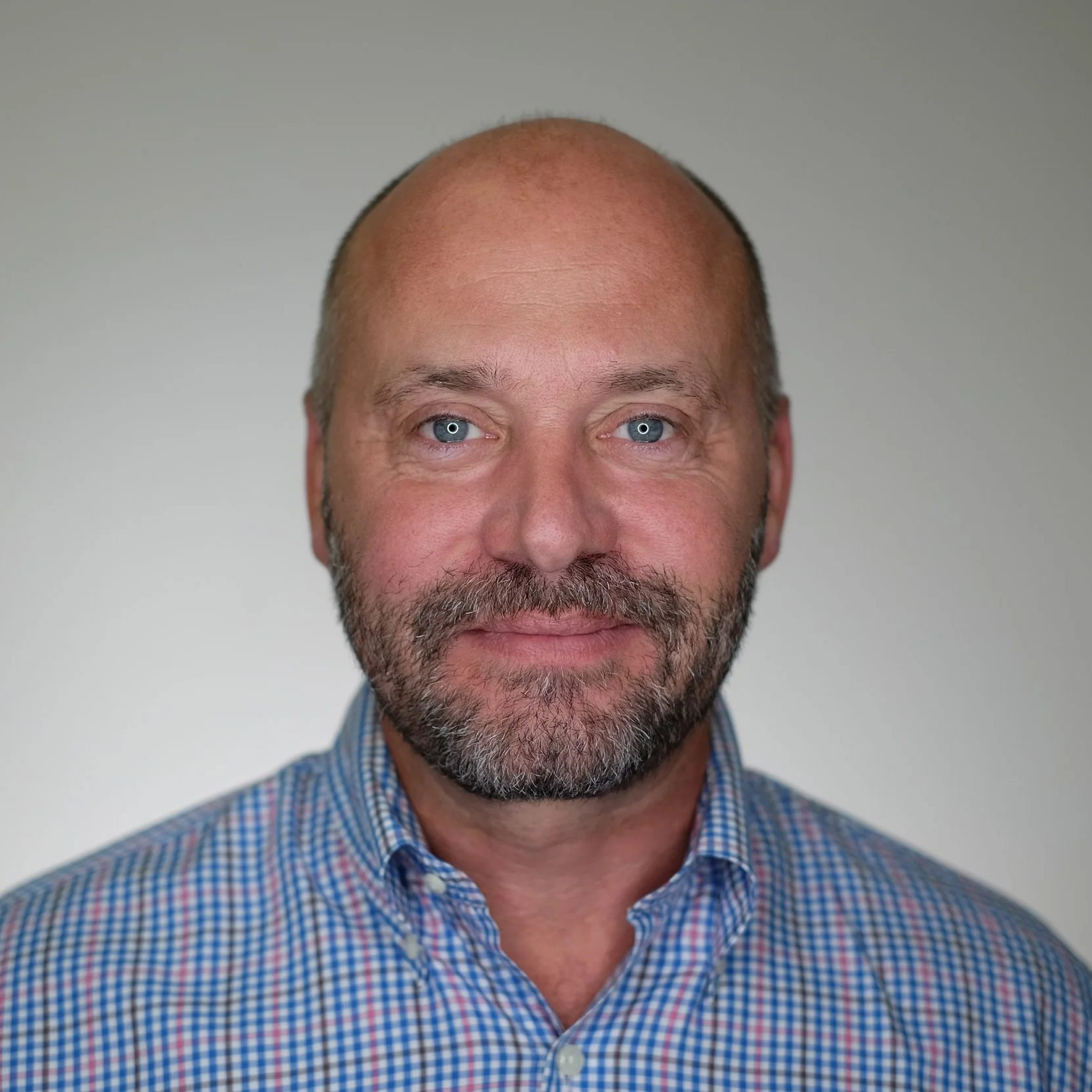 Head-and-shoulders portrait of a bald, bearded man with blue eyes wearing a blue plaid button-down shirt
