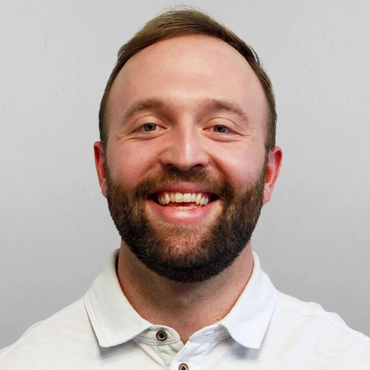 Smiling bearded man wearing a white polo shirt against a gray background
