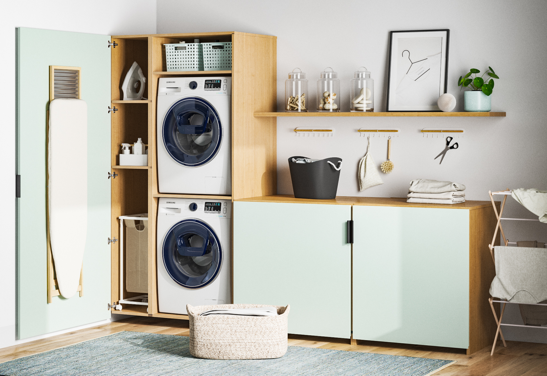 A modern laundry room with a light green cabinet, washing machine and dryer stacked, an ironing board on the door, shelves with baskets and jars, a black laundry basket, folded towels, and decorative items on a shelf.