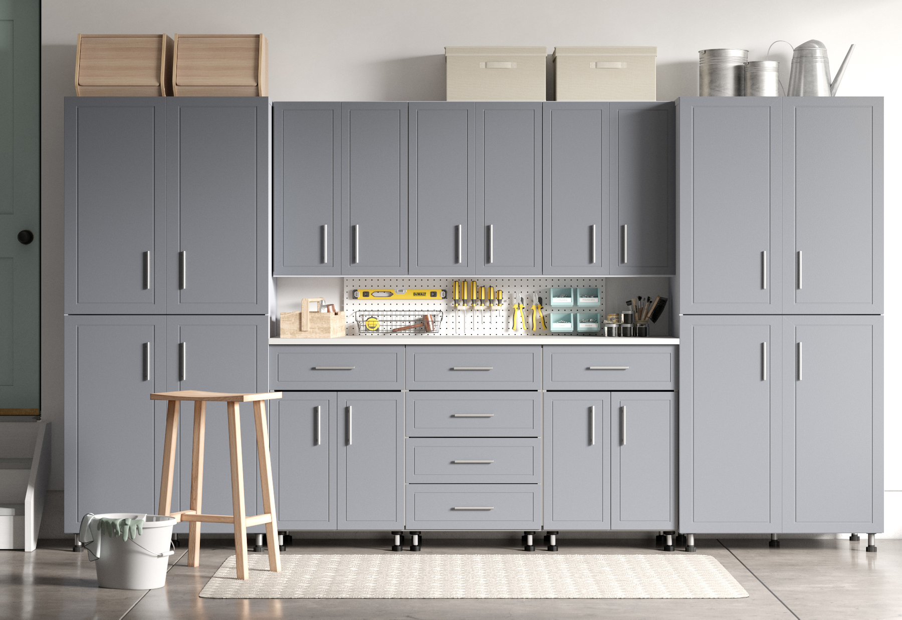 A gray garage cabinet wall with tools, storage boxes, and watering cans on top. A small stool and a white bucket are in front. The floor is wood with a beige rug.
