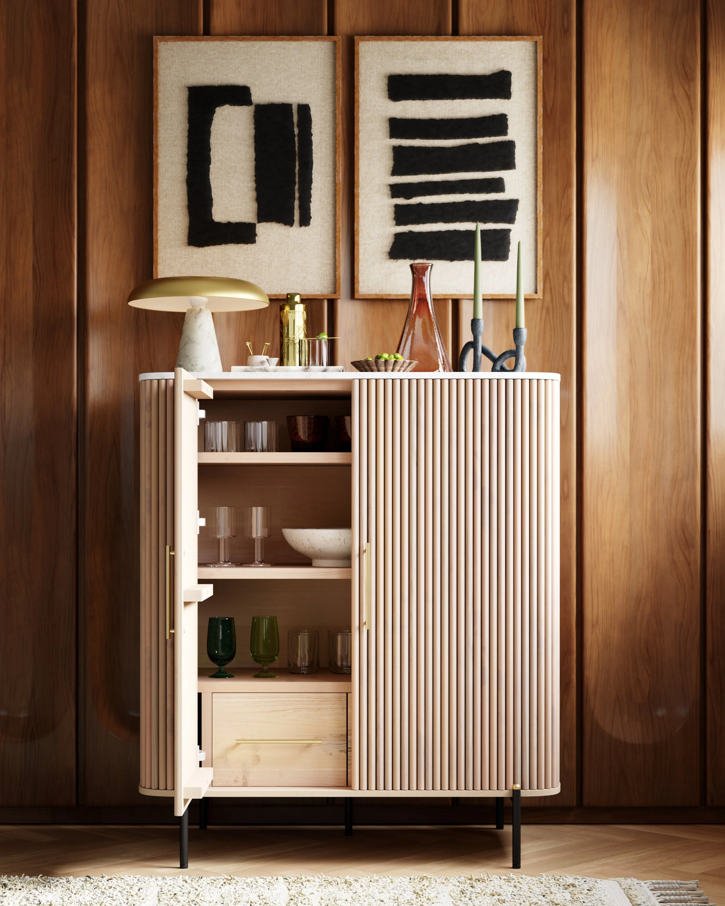 A modern wooden cabinet with open shelves and a sliding door, topped with decorative items like a marble-based lamp, a gold object, a brown vase, and green candles in black candleholders. Two abstract black-and-beige framed artworks hang on a wood-pa