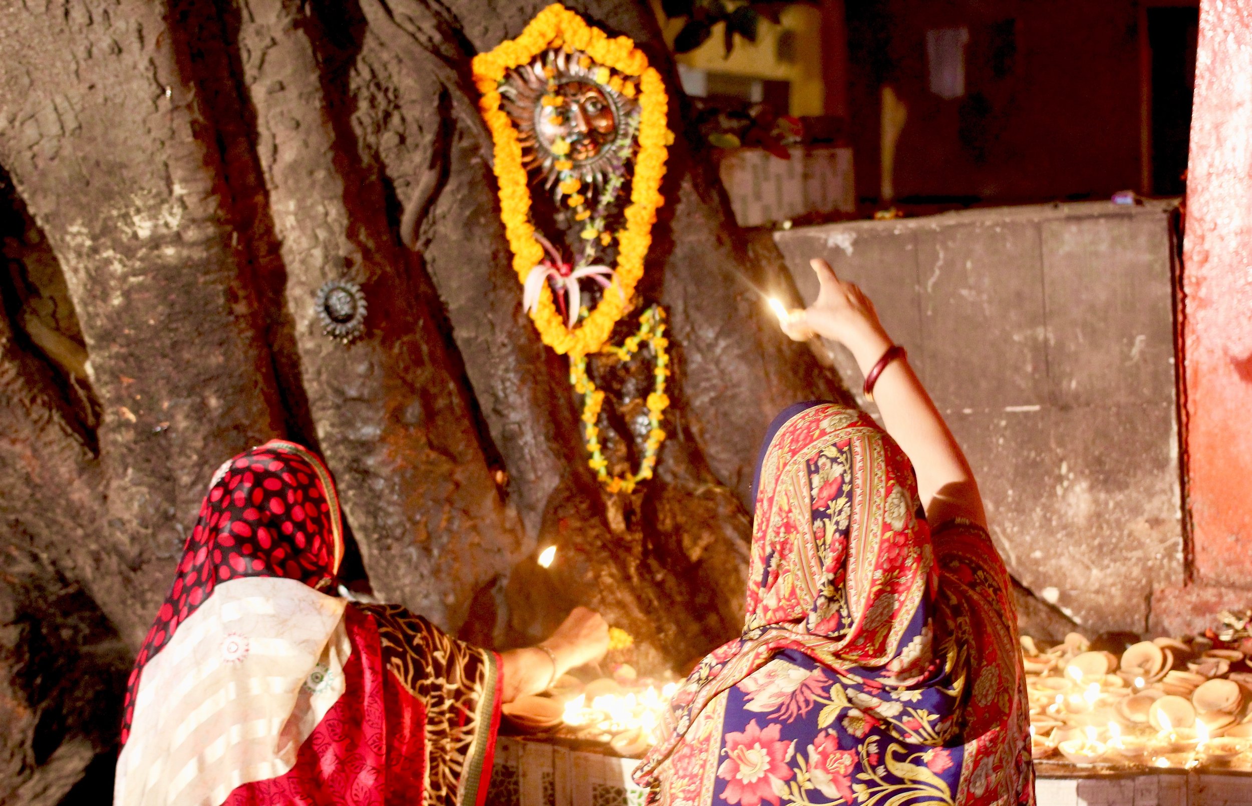 Women making puja (prayer) at a makeshift altar adorned with candles lit inside tiny ceramic bowls.