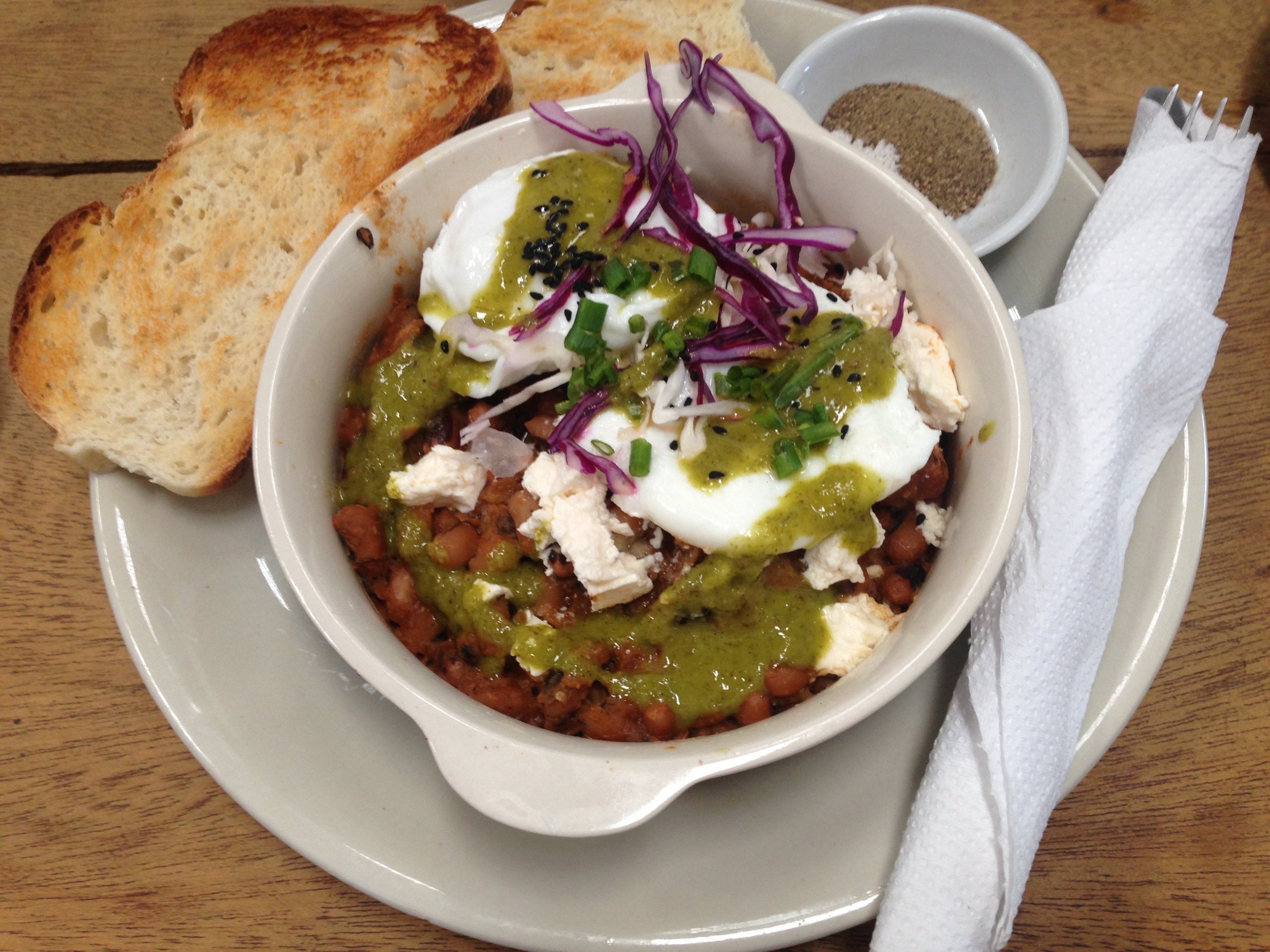 Poached egg drizzled in pesto sauce and black sesame seeds on a bed of thick beans