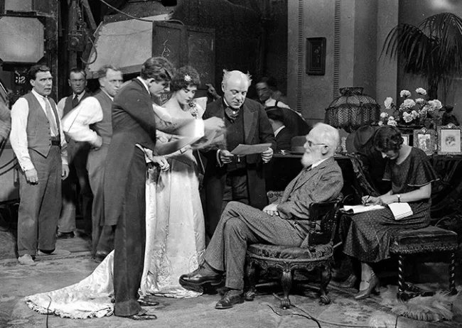 George Bernard Shaw, seated, speaks to actors on a visit to Elstree studios, where he watched the filming of his play How He Lied To Her Husband in October 1930.
