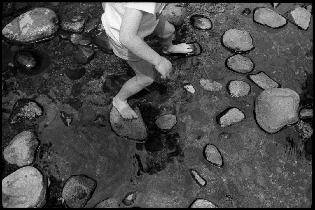 a black and white photograph of a child in a river with stones in the sierra nevadas of california