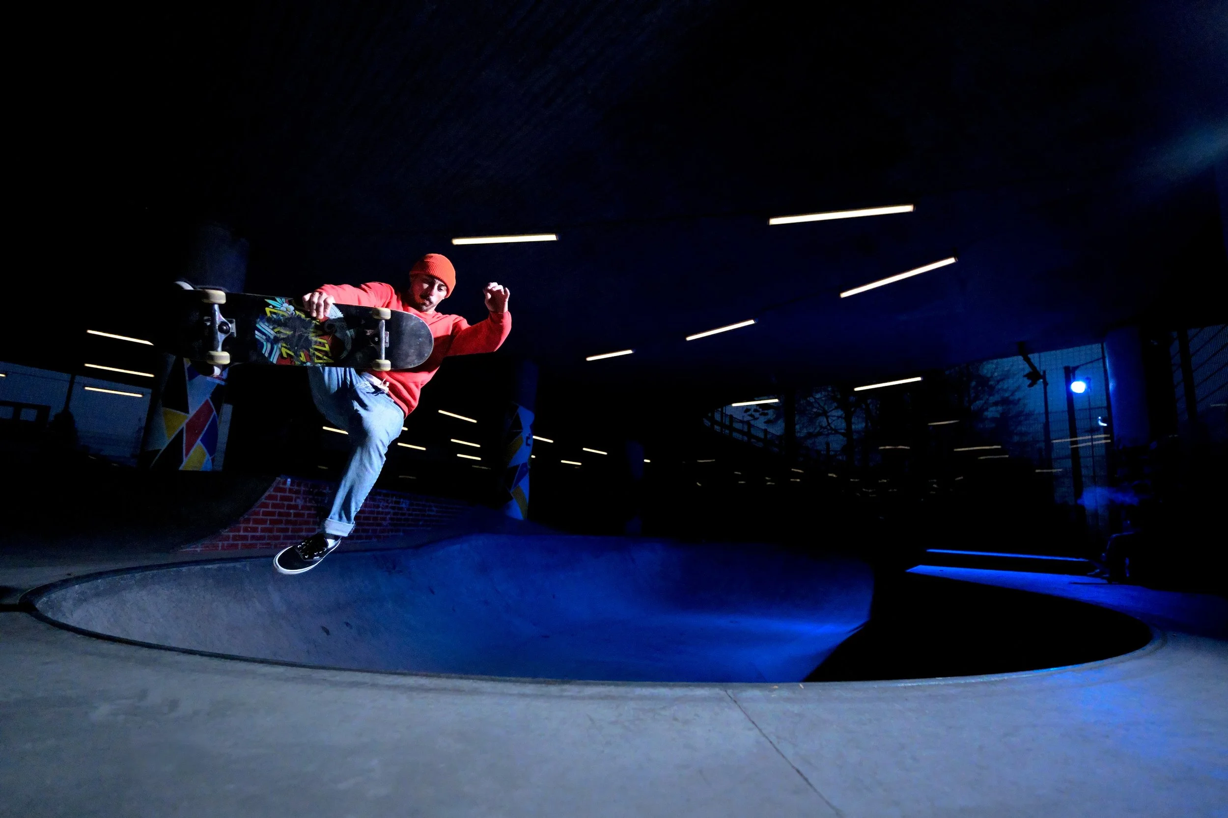 Skateboarder performing a trick in a skatepark at night, illuminated by overhead lights.