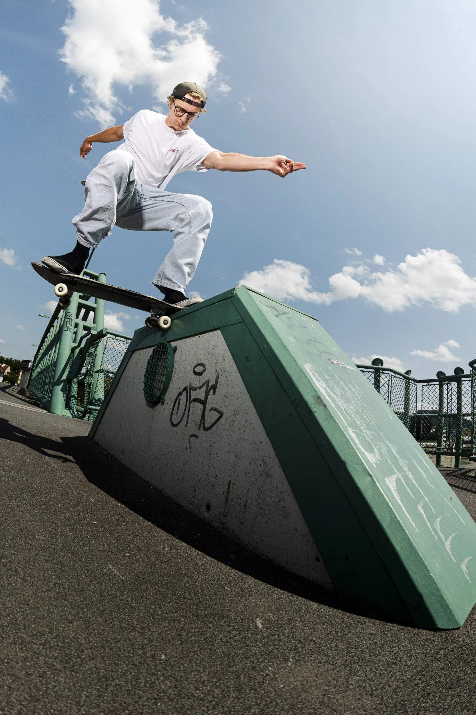 A young man skateboarding outdoors on a sunny day, performing a trick on a green ledge at a skate park.
