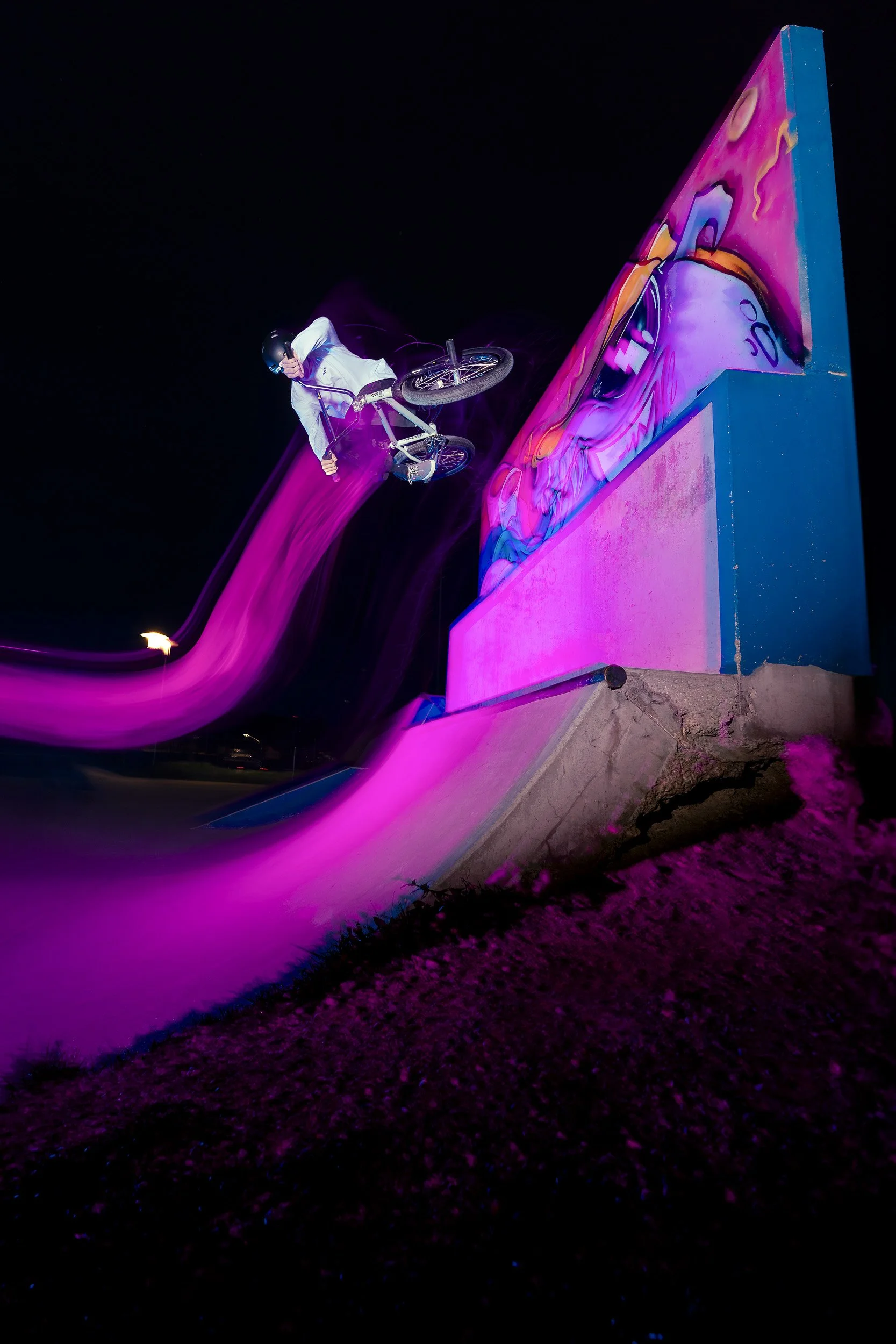 A BMX rider performing a stunt off a skatepark ramp at night, with colorful neon lighting.