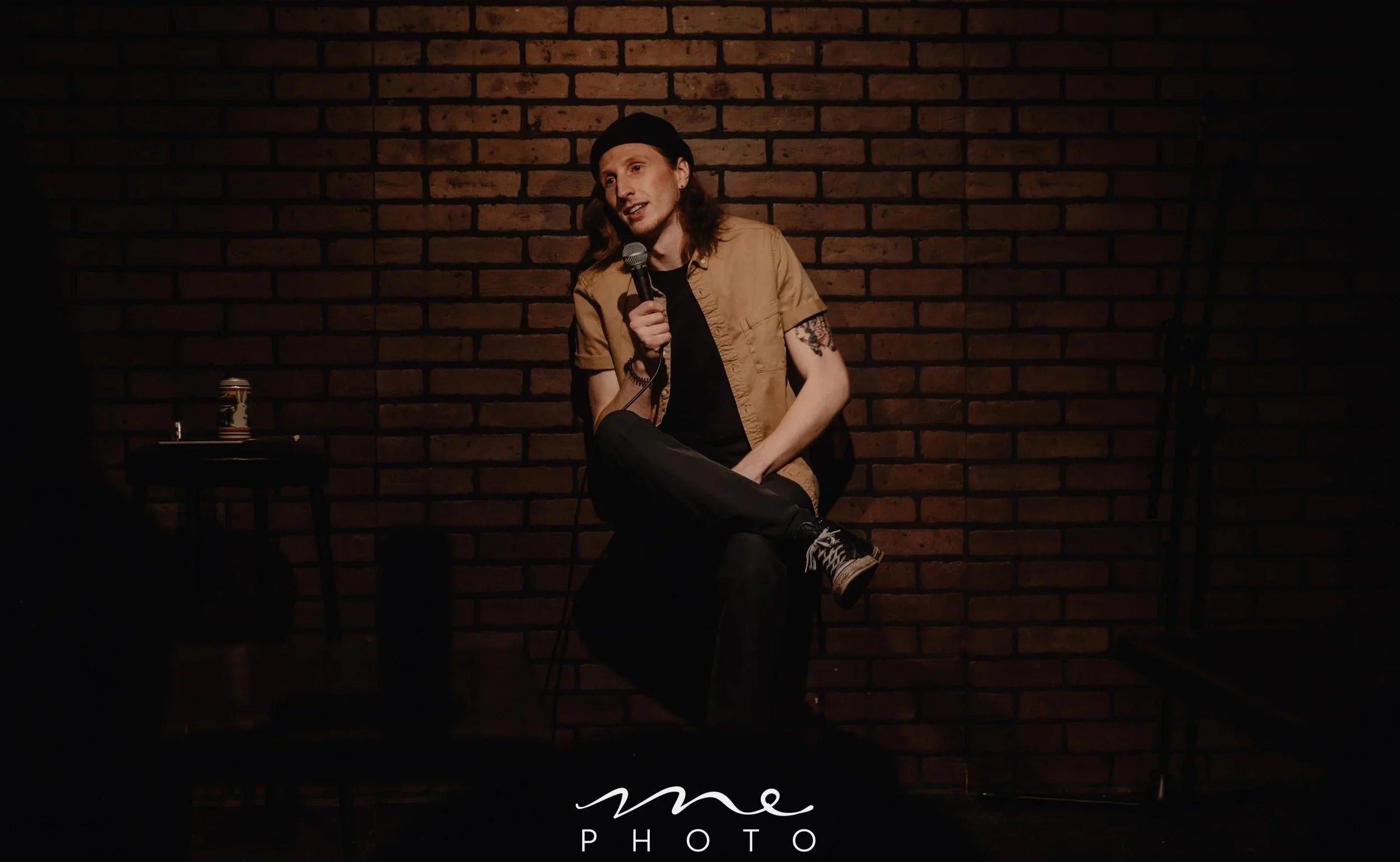 Conner Christmas performing at Good Times Comedy Club in Lethbridge, Alberta. Photo by Me Photo. Conner is leaning against the back wall of the stage pretending to sit down.