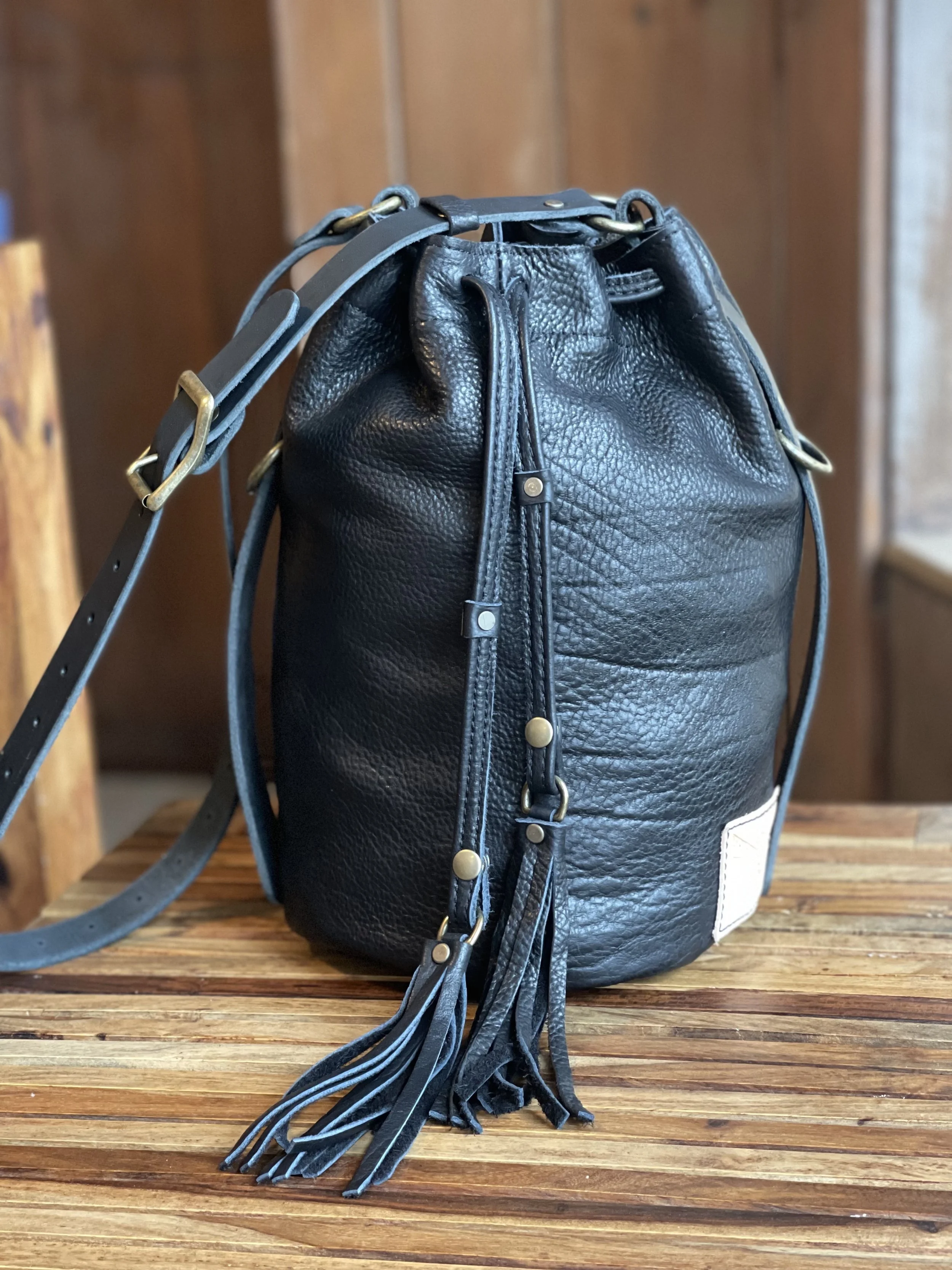 LILI BUCKET BAG IN BLACK BISON LEATHER WITH REMOVABLE BLACK BISON FRINGE PULLS AND ANTIQUE BRASS HARDWARE.
