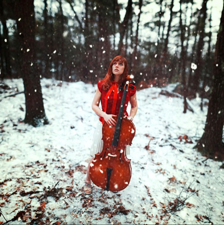 Cello instructor Amanda standing in a snowy forest holding her cello in Merrimack NH