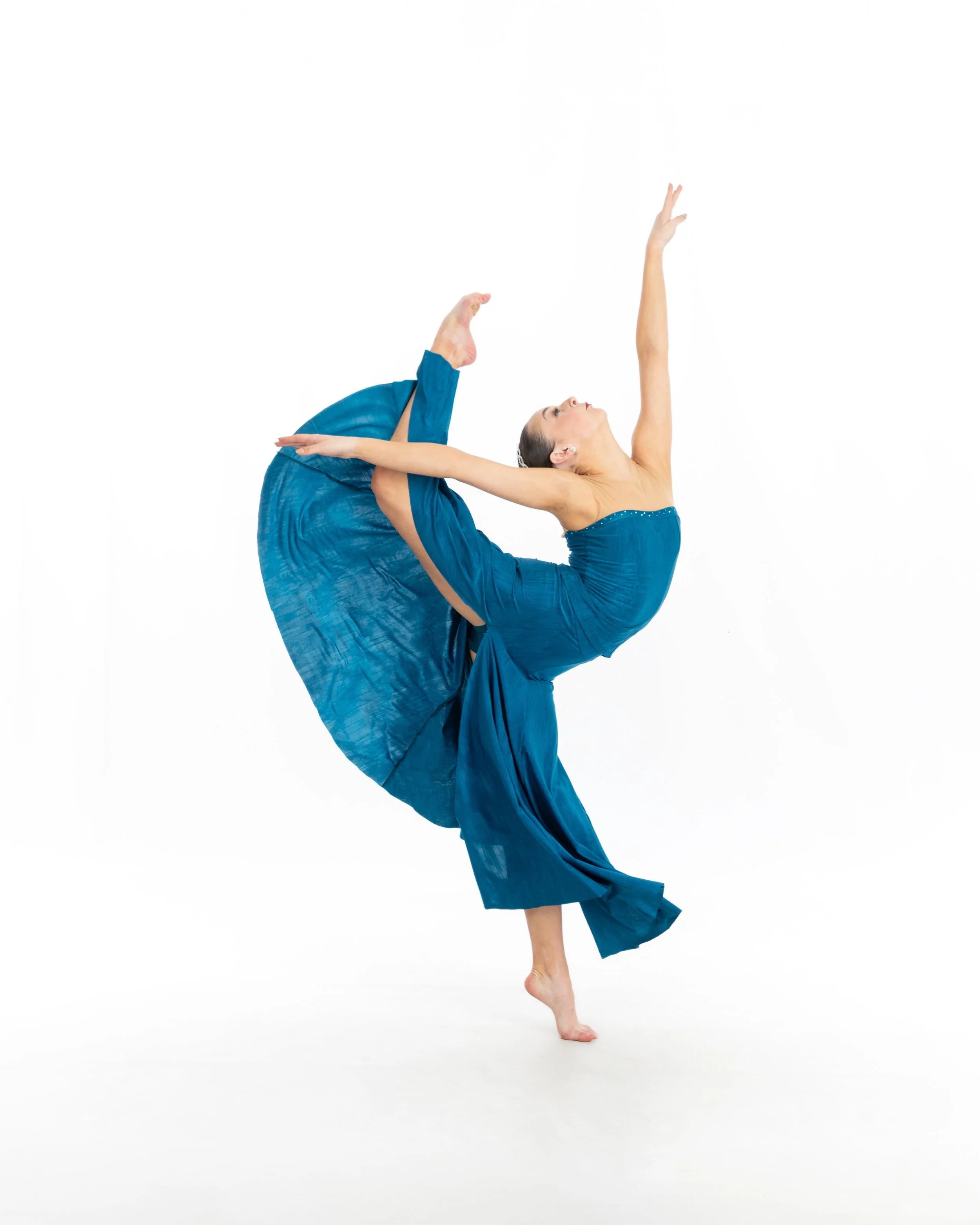 A woman performing a dance pose in a flowing blue dress against a white background.