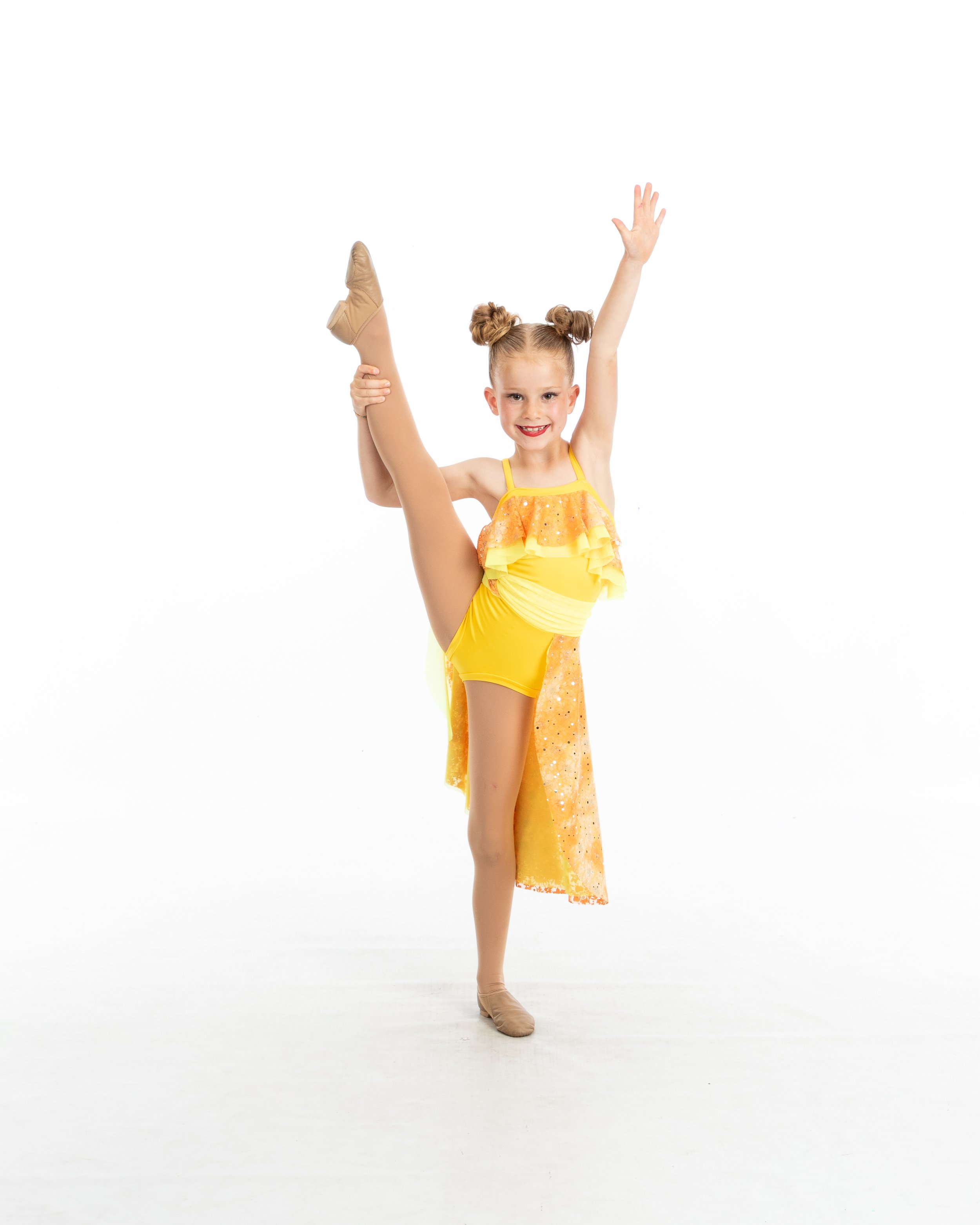 Young girl in yellow dance costume performing a standing split with one arm raised and a smile.