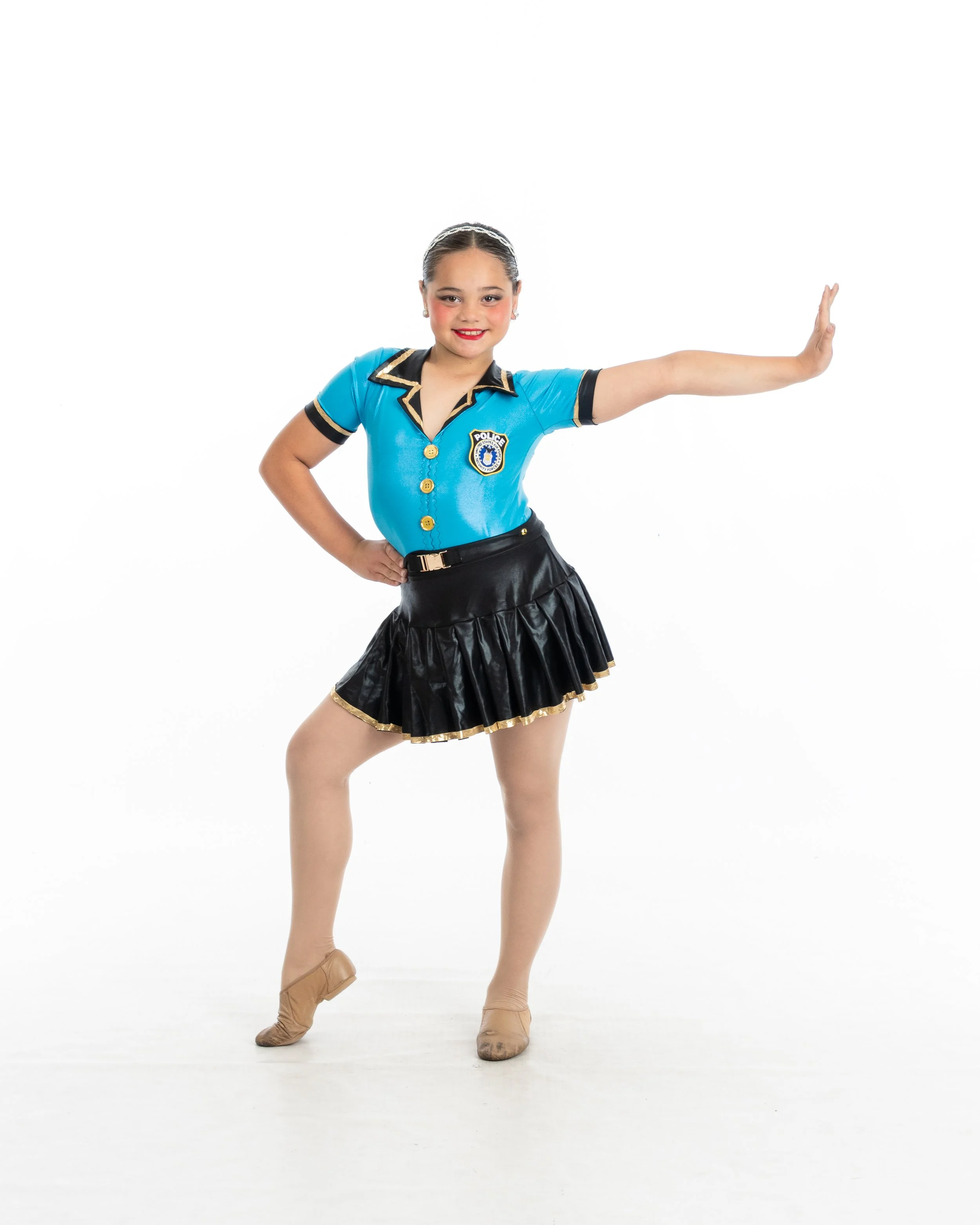 Young girl in a police-themed costume performing a dance pose, standing with one hand on her hip and the other arm extended outward, smiling against a white background.