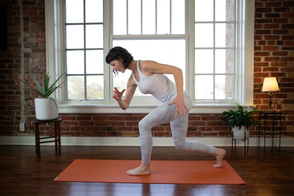 Woman practicing yoga indoors on an orange mat near large windows with brick walls and potted plants during her personal branding photoshoot in Lisbon.
