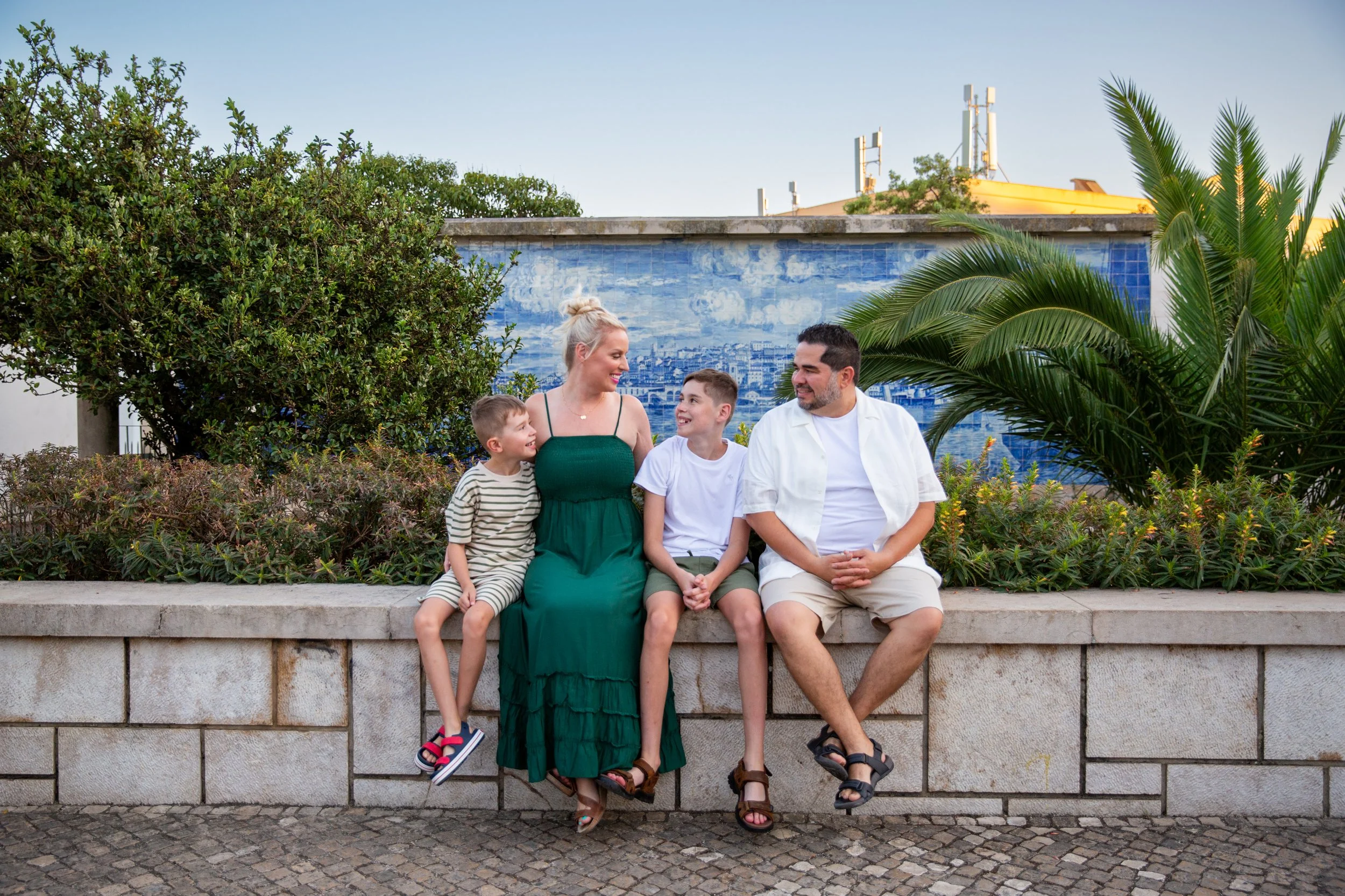 Family photoshoot in the Lisbon neighborhood of Alfama, with all four family members sitting on a wall in front of a Portuguese tile wall.