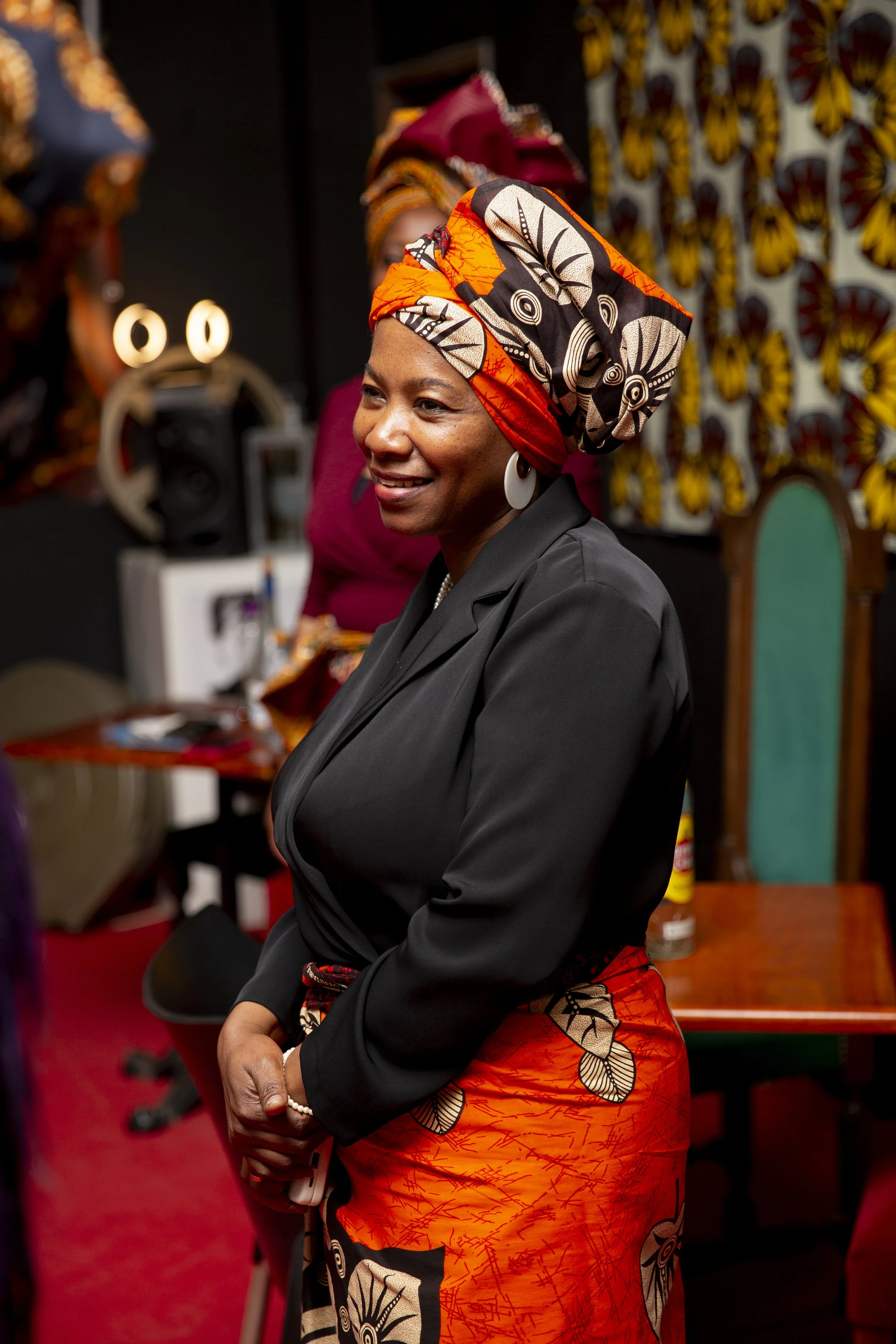 A woman in colorful traditional African attire and headwraps, standing on a red carpet at an event, during a branding photoshoot for clothing company in Portugal.