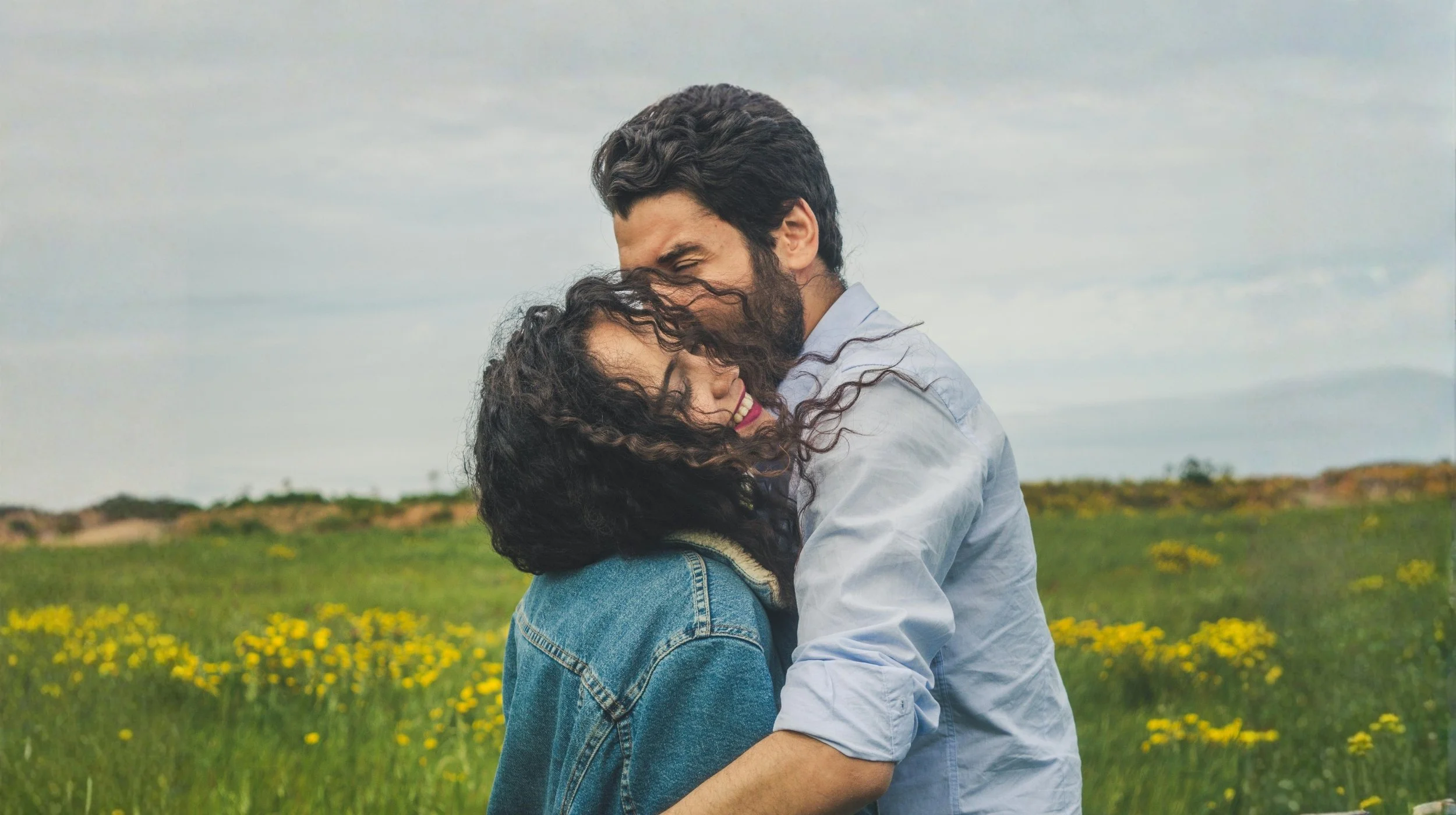 Couple embracing in a grassy field with yellow wildflowers, sharing an intimate moment that represents connection and relationship healing.
