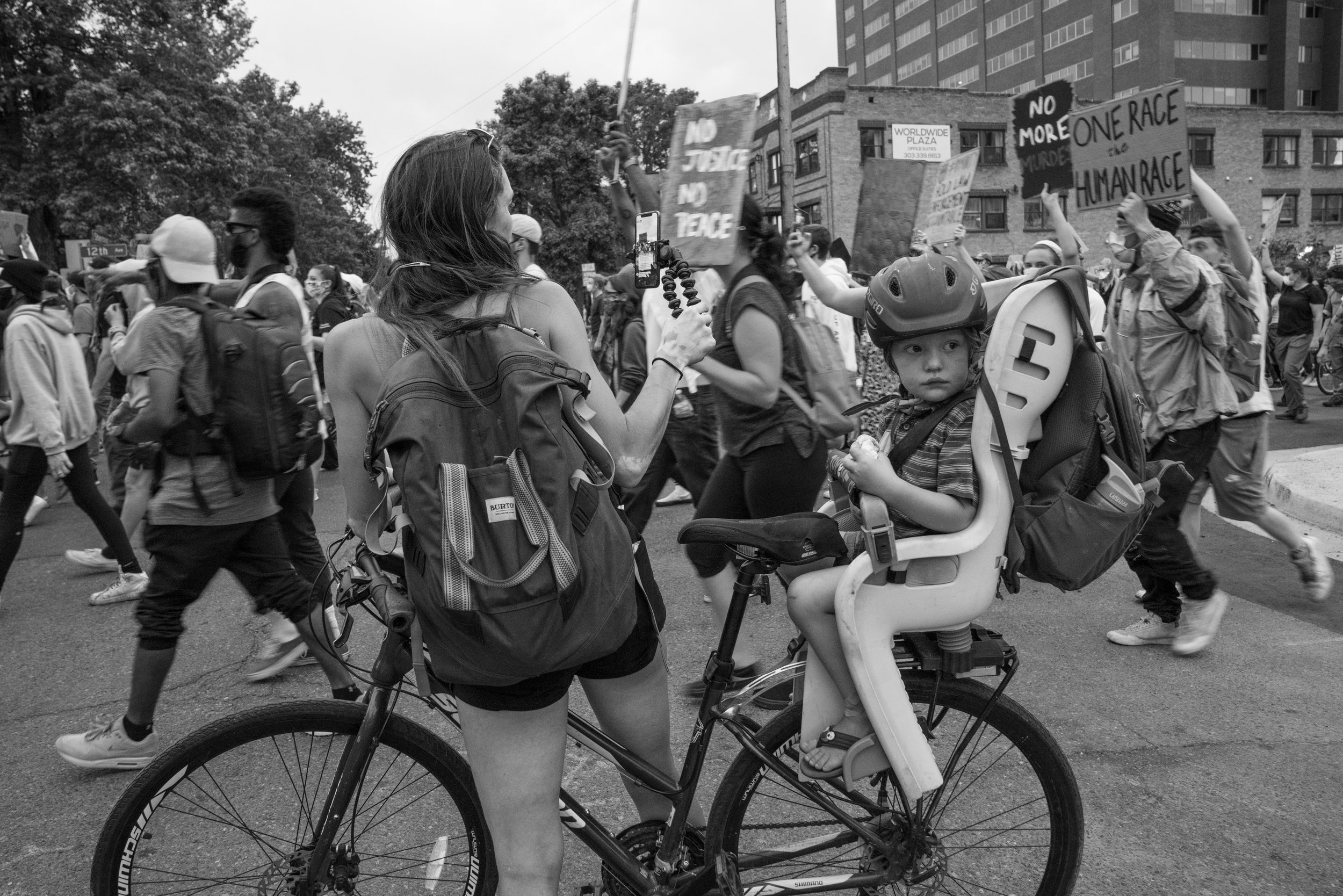 Protesters march through downtown Denver as a child in a bike looks the other way. 6/02/2020.