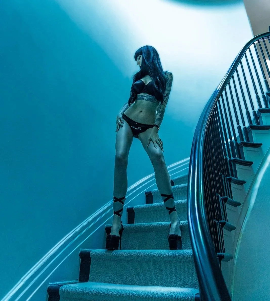 Ramona Ryder posing on blue staircase in black lingerie and heels