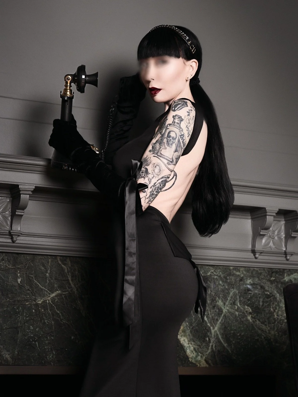 Goth NYC Escort Ramona Ryder is wearing a black d ress with her hair pulled back with dark red lipstick holding an antique phone.