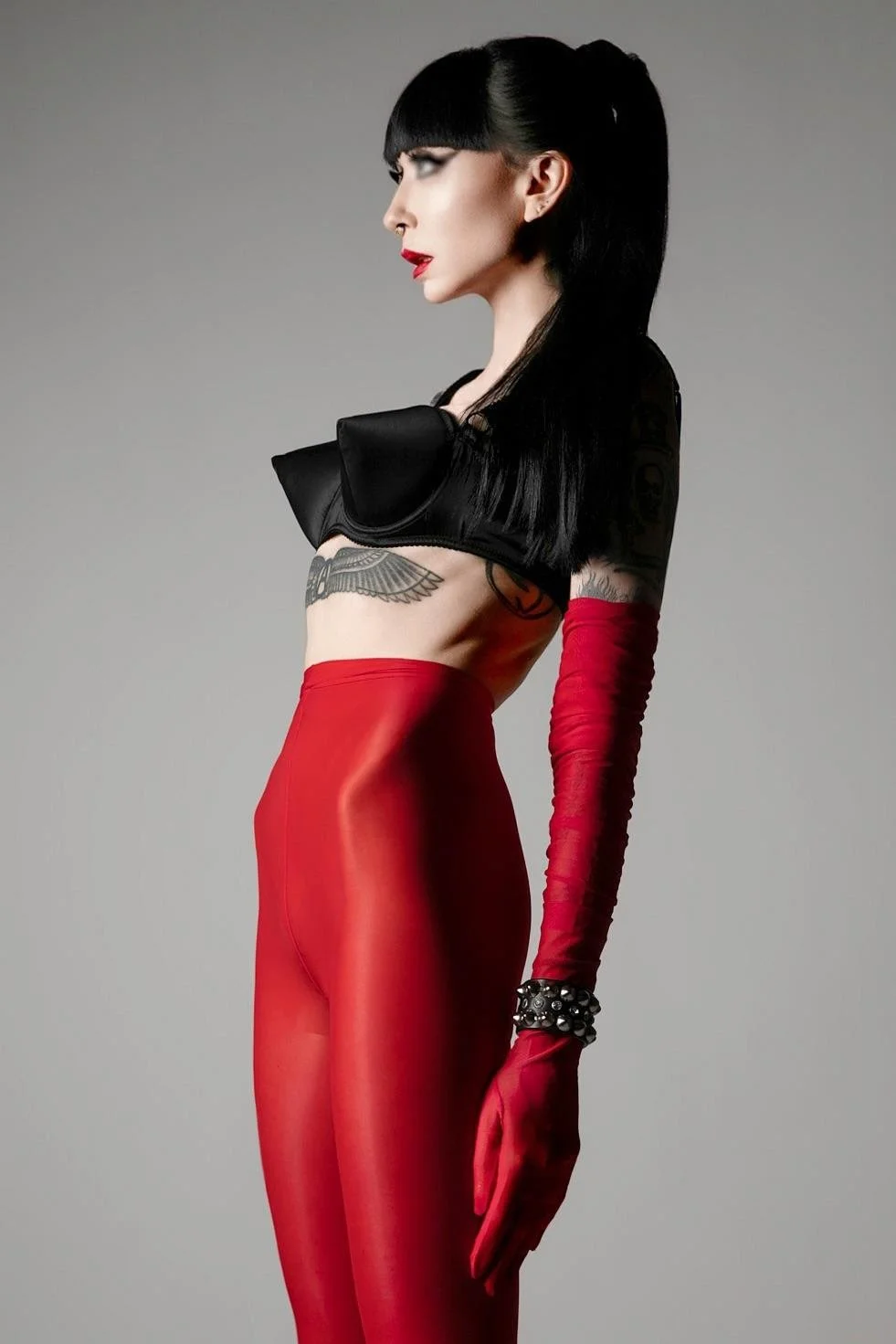 NYC Ramona Ryder is wearing a black bullet bra and red nylons with red opera gloves.