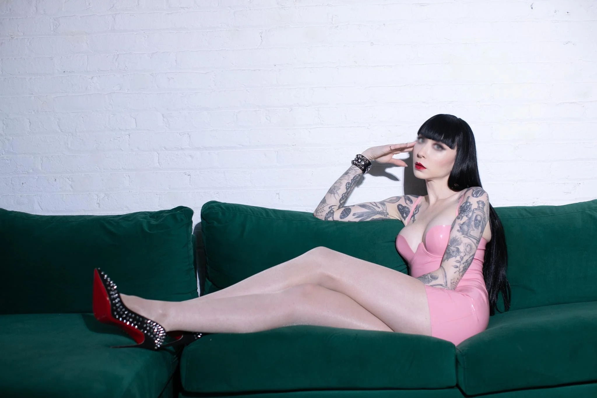 Ramona Ryder is wearing a pink latex dress sitting on a green couch