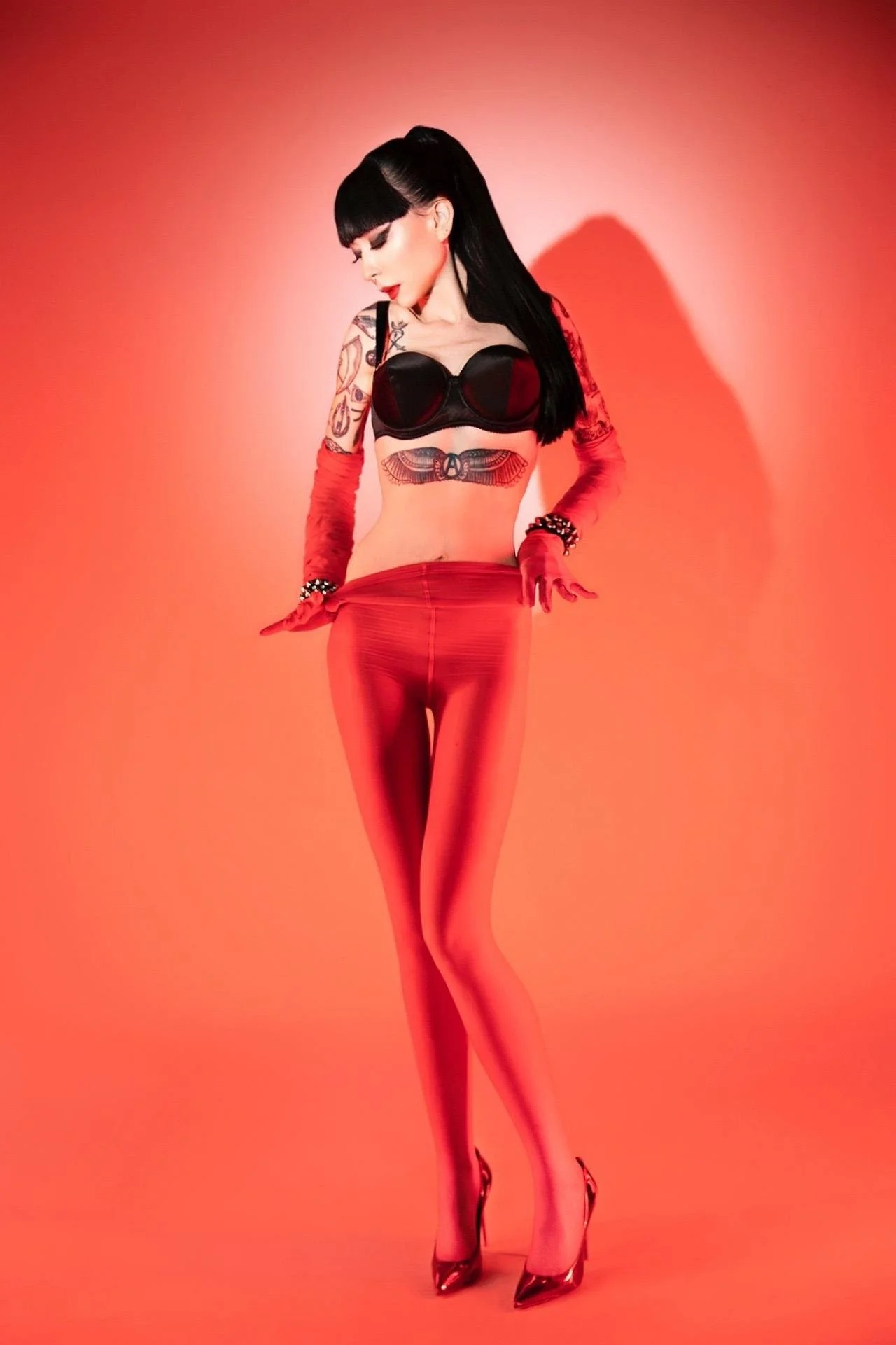 NYC Ramona Ryder is wearing a black bullet bra and red nylons with red opera gloves.