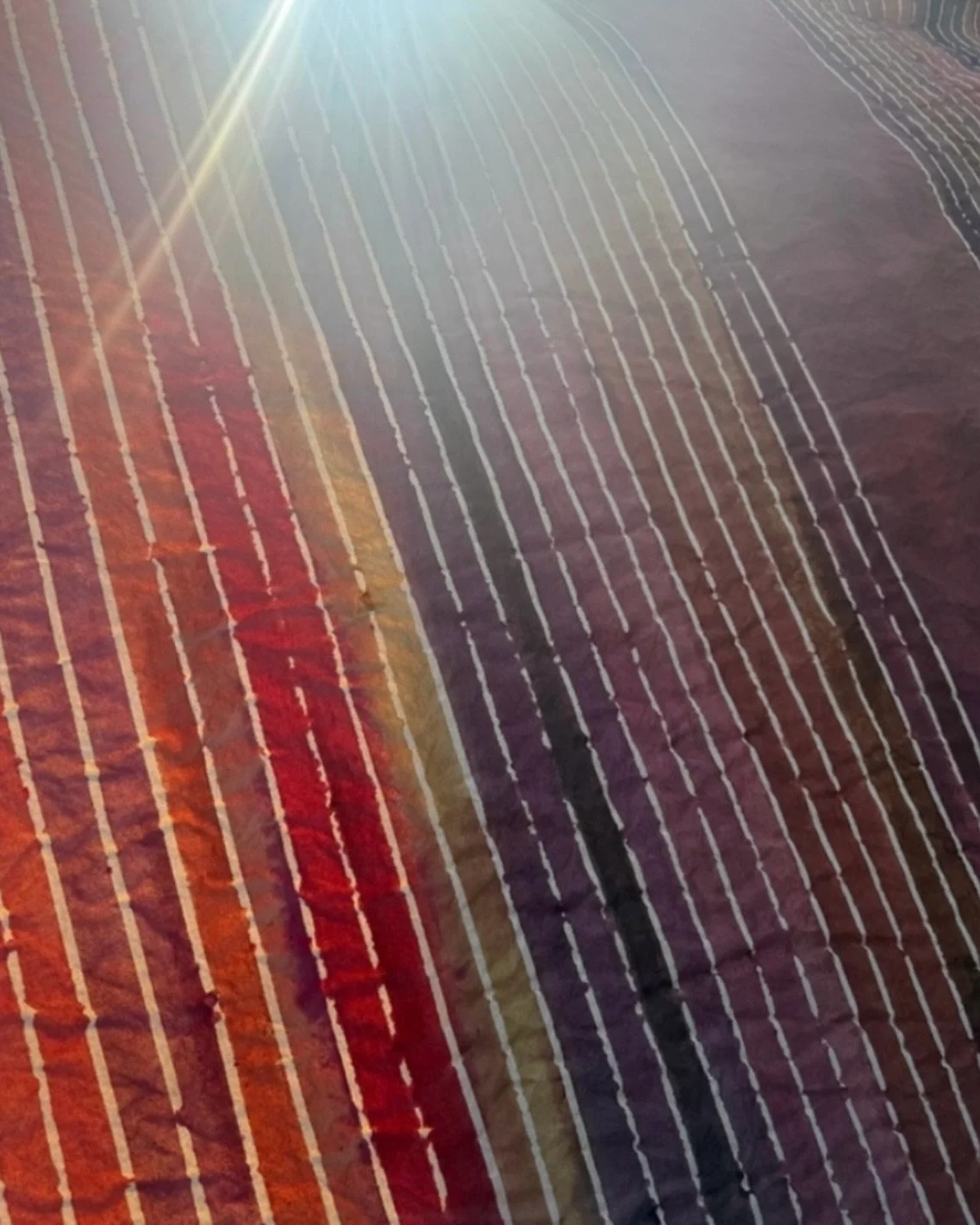 On cloth, color behaves differently than it does in the jar. It moves. It resists. It pools along stitched lines and fades where the fabric is tight. A sharp stripe softens. A flat wash becomes atmosphere. What looks controlled from afar is, up close