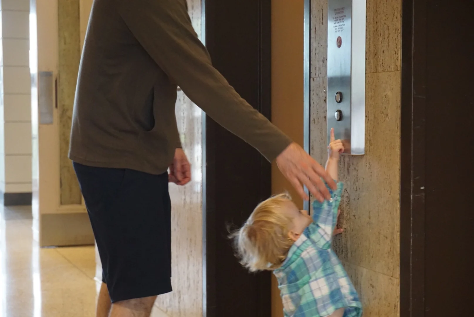 With a little help from Dad, Leo pushes the "UP" button to call the elevator.