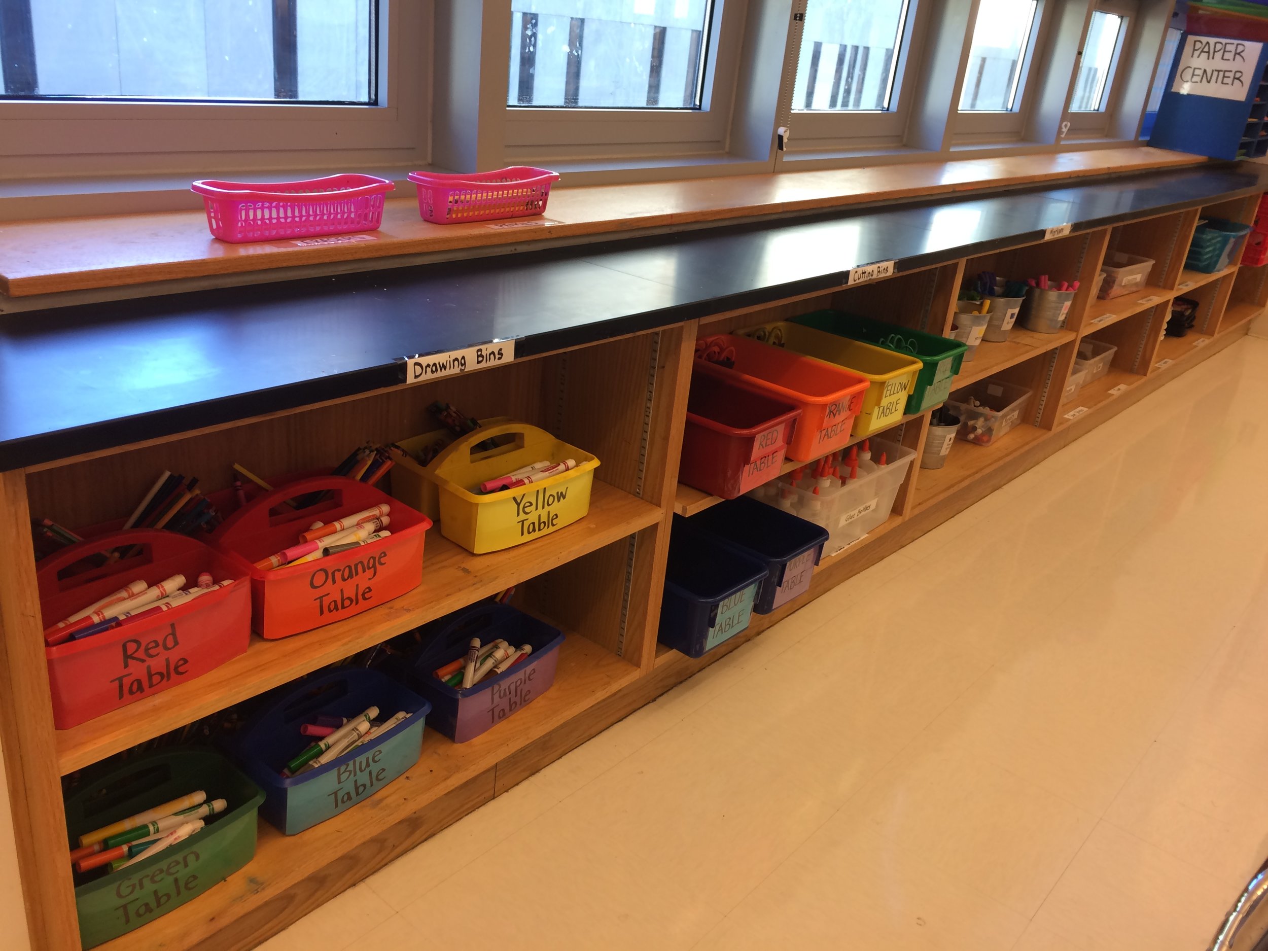 The table bins are color coded to match the tables and I table where they go so kids can easily get and put back. I make two bins for each table, one with drawing materials and one with glue and scissors for cutting. 