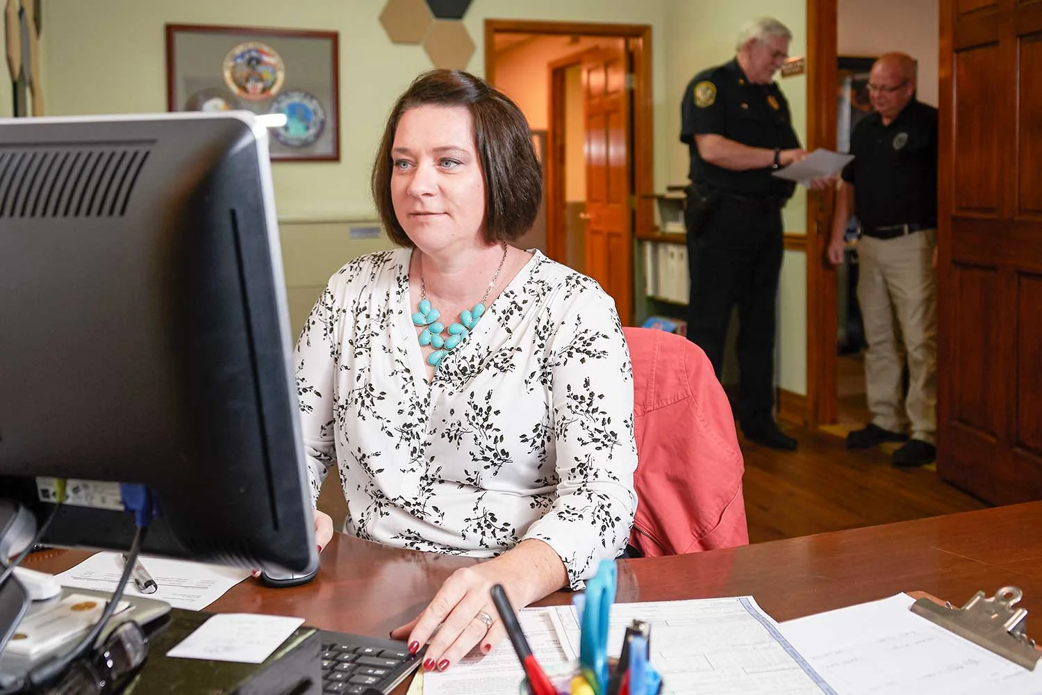 Wilmore Police Administrative Assistant Kim Stewart enters information into her computer as Chief Bill Craig and Officer Sam Hensley talk outside the chief’s office.(Photo by Jim Robertson)