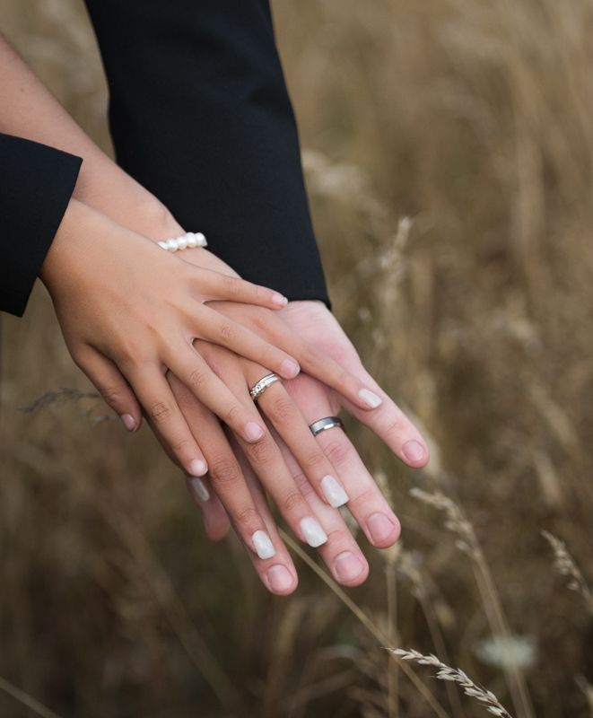 Bride and groom hands with child outdoor wedding in tall grasses