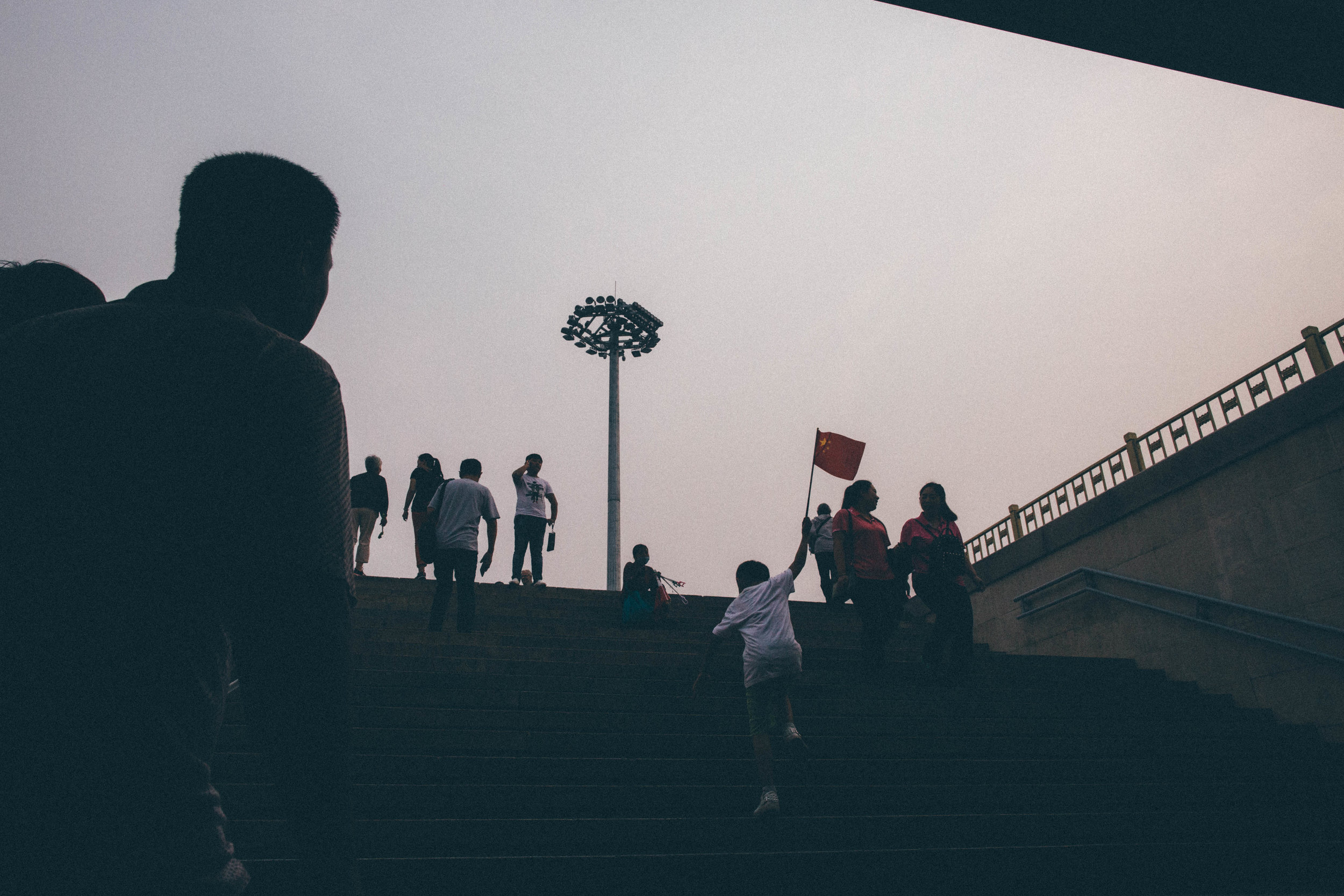 A young boy runs up the stairs to Tiananmen square waving the flag of the People's Republic of China. Beijing, China. 