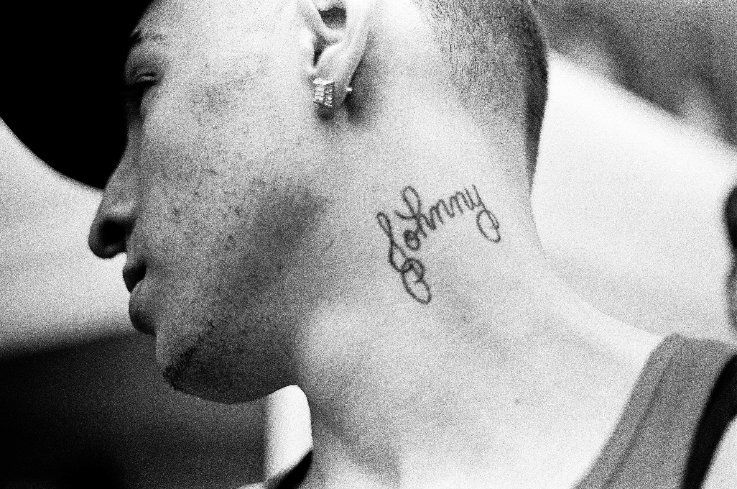 A young man shows off a neck tattoo that reads "Johnny" 