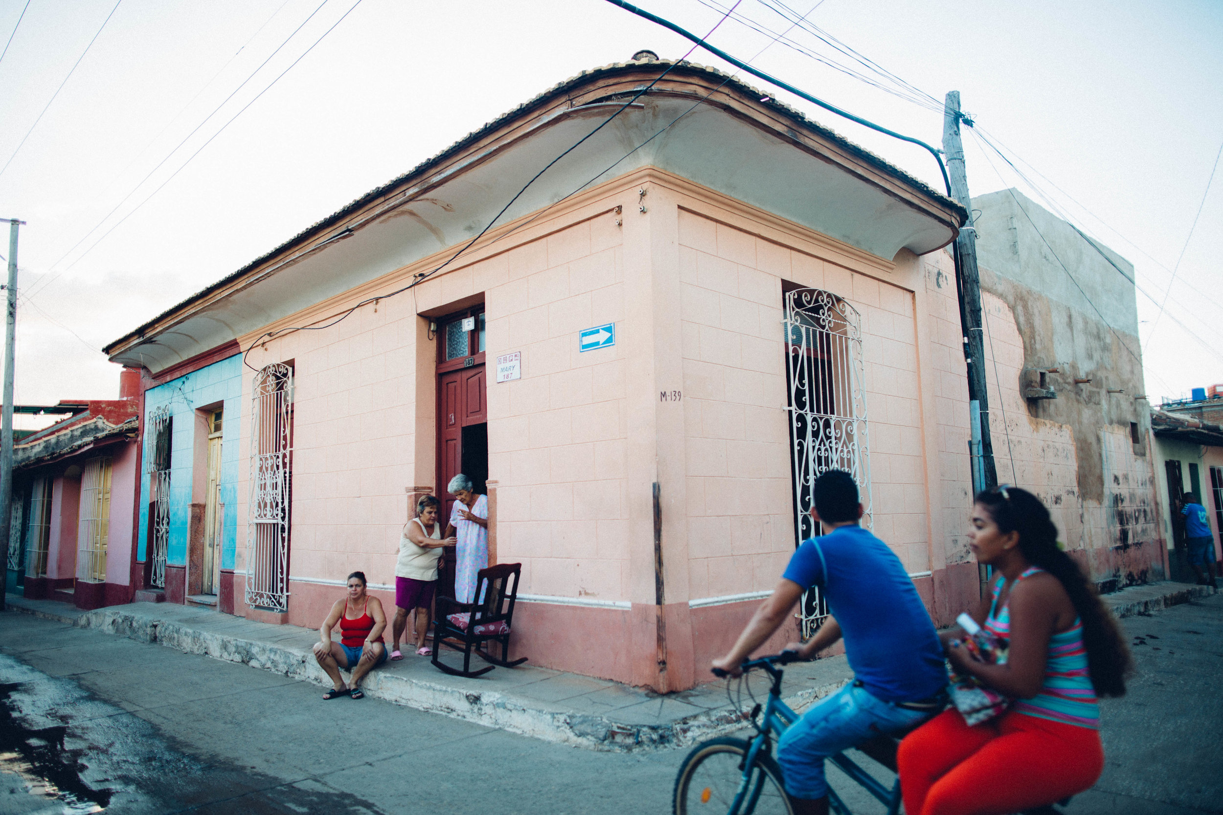   A daughter, a mother and a grandmother congregate outside their home in Trinidad as a young couple rides past on a bike. Trinidad, Cuba.  