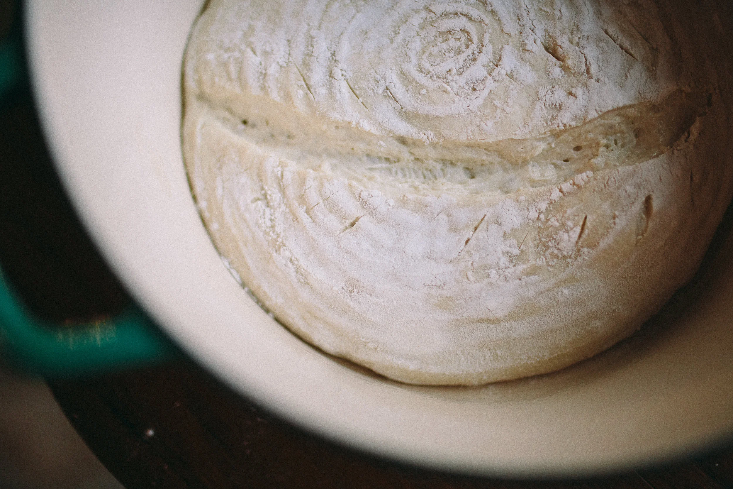 “11.5 After the dough has risen to twice its original size, it gets shaped into loaves (not pictured -- we didn't have time to wait three hours for this to happen!) and goes for a cold proof in the fridge, usually overnight (also not pictured). This gives the loaves a bit of a tougher skin, which makes it easier to make lovely slash marks in a pattern on the loaf. All you really need is one good slash through the middle; this lets steam escape from the loaf as its baking. If you don't slash a loaf, the steam will escape through the path of least resistance, which sometimes makes these lovely break patterns on the top of the loaf, but sometimes means it breaks through the side or the bottom of the loaf, so slash patterns are generally more dependable.”