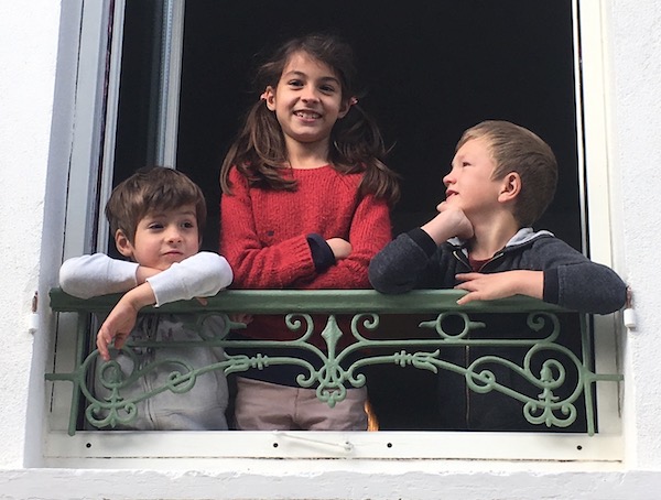 The grandchildren waiting at the window of their house around the corner.
