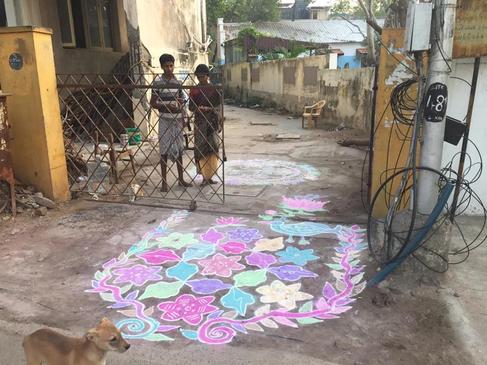 Here's my friend (I don't know her name yet as we don't speak the same language) and today's beautiful rangoli. If you recall, rangoli is another type of yajña, an offering for the well-being of the home, neighborhood, and nearby people. I have kept up my tradition of bringing her a little gift each day, to return the happiness that she brings me with her beautiful art. Yesterday I brought her 3 tangerines (she usually has two girls with her) and today I brought her 3 candy canes I brought from Texas. Her face lights up with each little gift. It might just be the best part of my day. Notice that this one has a pretty blue bird and a big lotus flower just inside the gate. The lotus flower symbolizes rising up out of the mud and becoming something beautiful. I walked by again on my way home from lunch and she showed me the book she was using to plan tomorrow's rangoli. <3