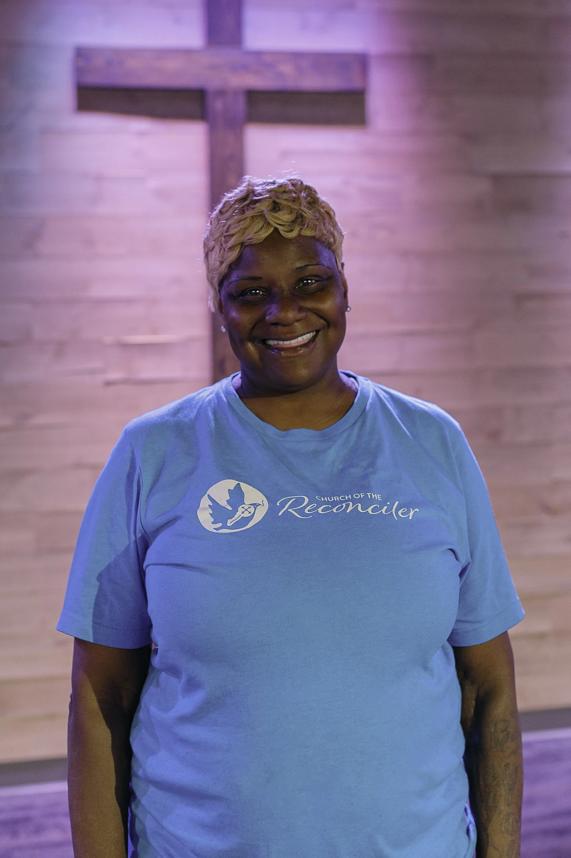 Pam wears a big smile and her light blue COTR T-shirt with white lettering and dove & key logo