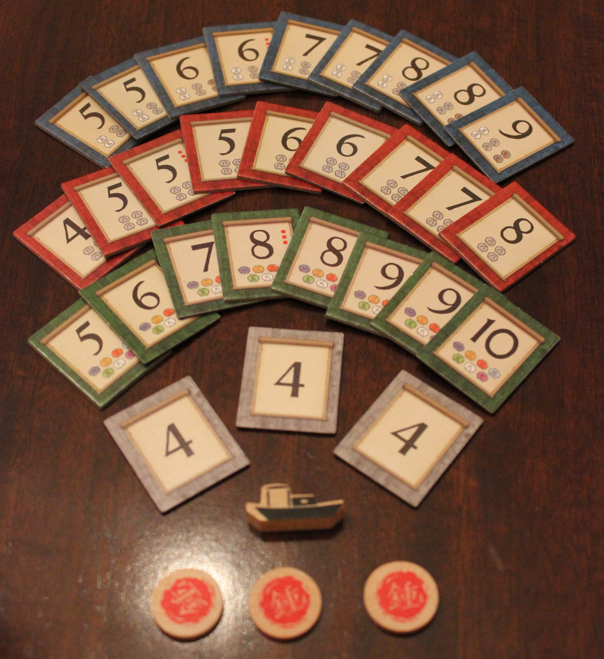 The three sets of devotion tokens that act as points for the end of the game. There are three "wilds" that give 4 points if any stack runs out. Also pictured: first player marker (a boat) and some favor tokens.